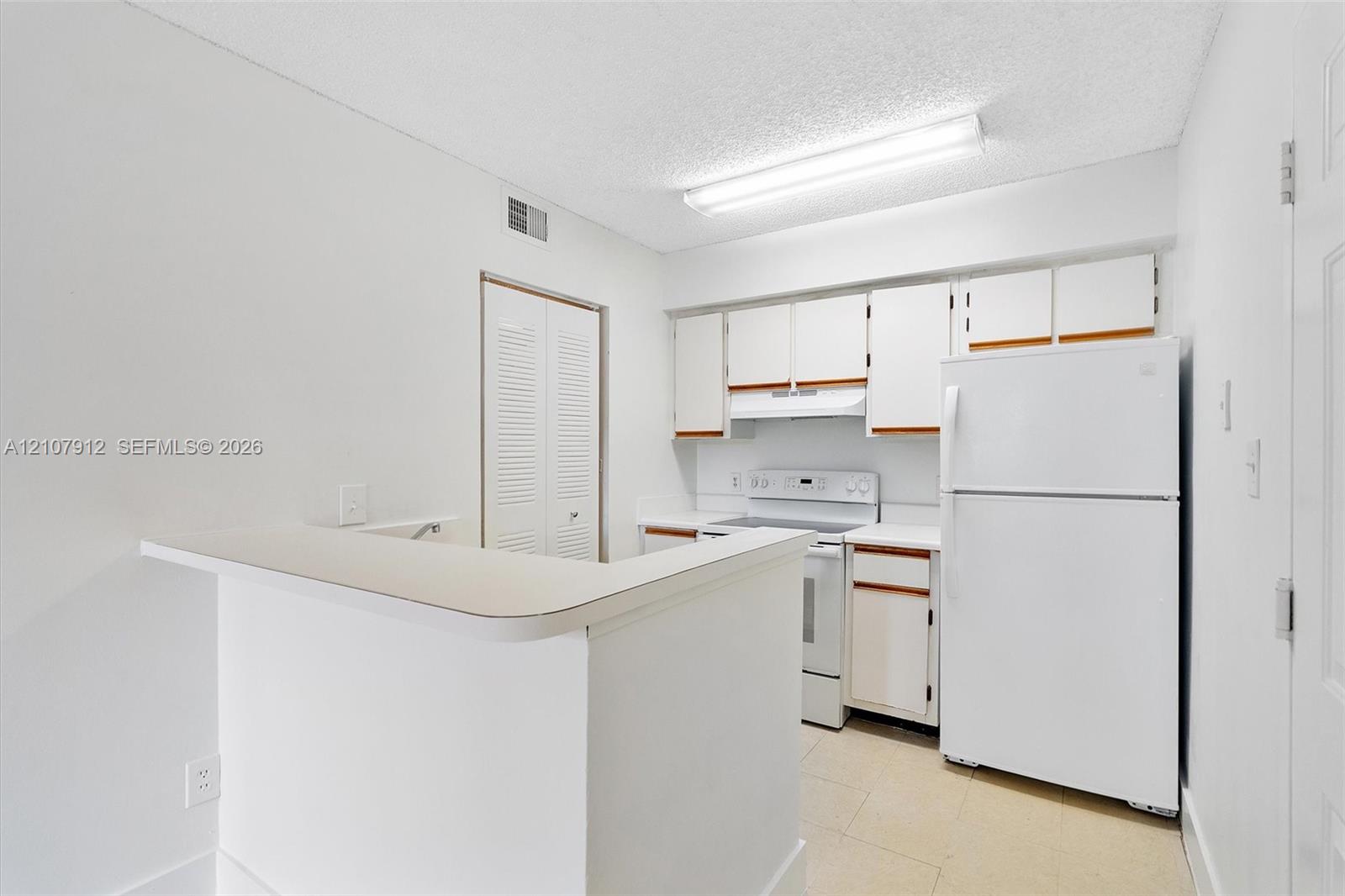 Kitchen featuring white cabinetry, solid-surface breakfast bar, tile flooring, and integrated white appliances