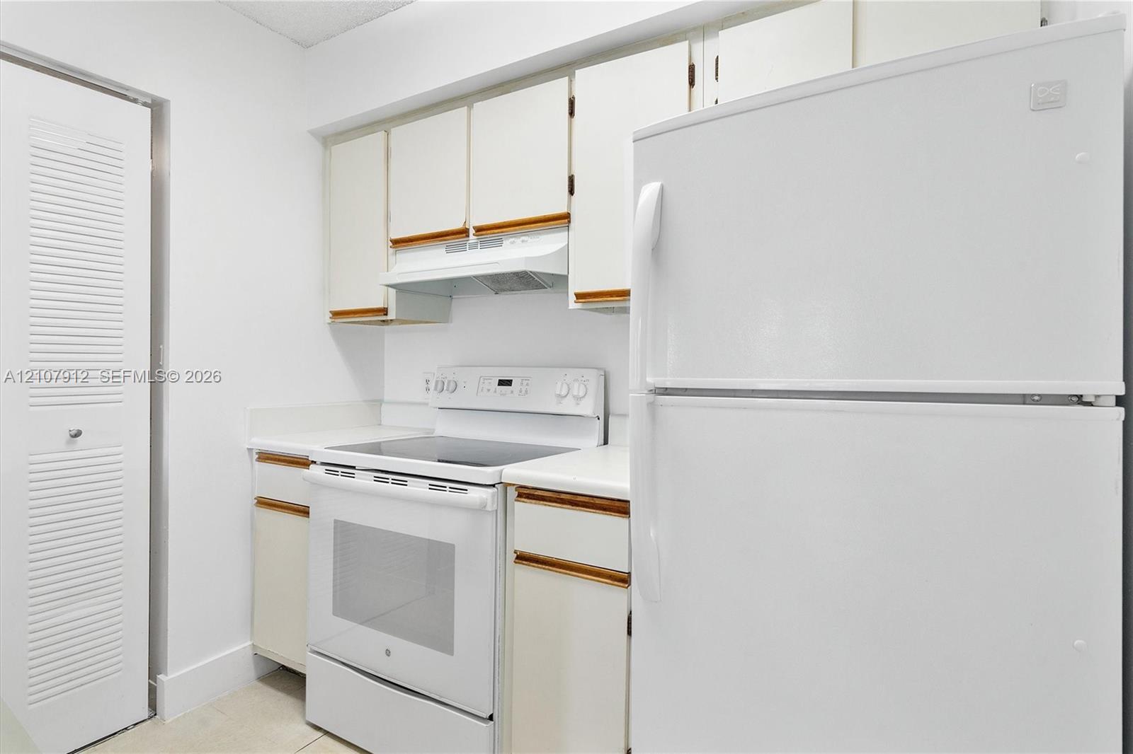 Kitchen featuring white cabinetry with wood trim, a built-in exhaust hood, a white electric range, a full-sized refrigerator, and a louvered-door closet