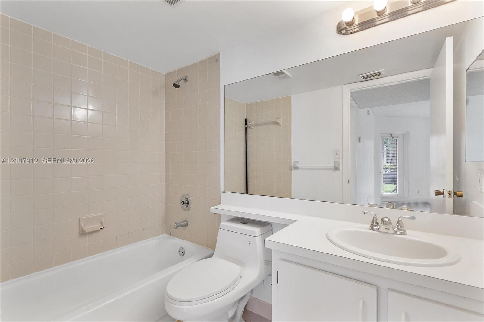 Bathroom featuring a white vanity with a recessed oval sink, expansive wall-to-wall mirror, one-piece elongated toilet, and a tiled tub-shower combination