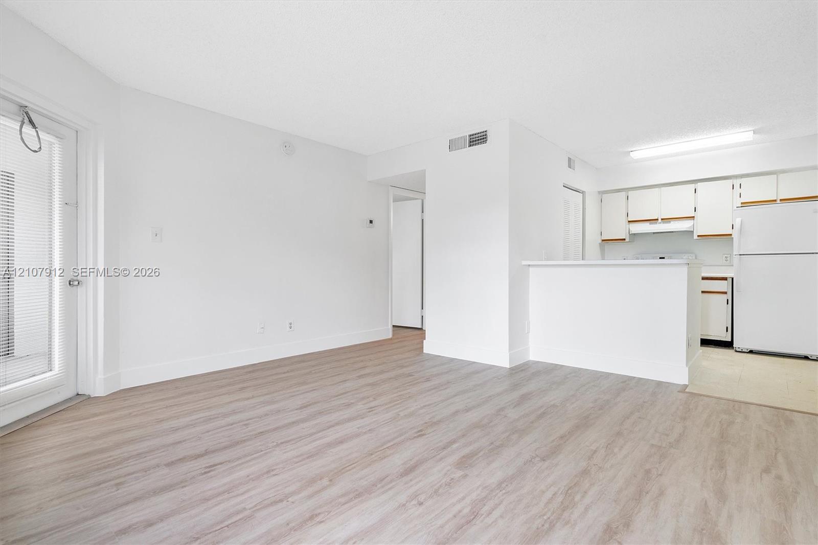 Open living space featuring wood-finish flooring, white cabinetry, a kitchen pass-through counter, and a glass-paneled entry door