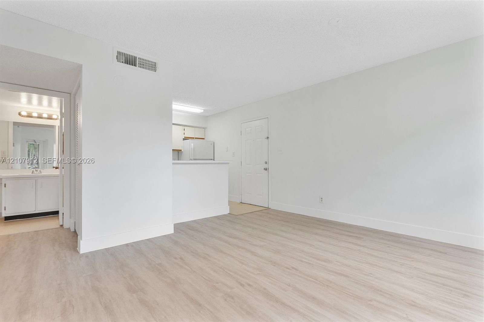 Neutral interior space featuring wood-finish flooring, white walls, and a pass-through opening to the kitchen area