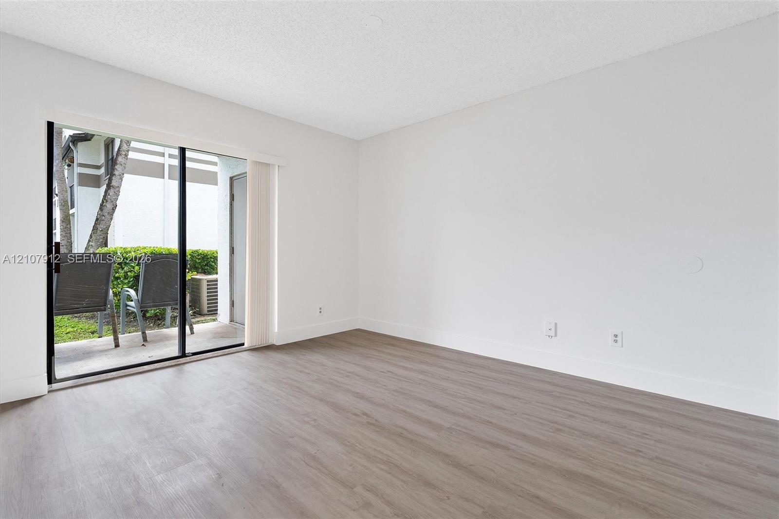 Neutral-toned walls, wood-finish flooring, and sliding glass door opening to a concrete patio