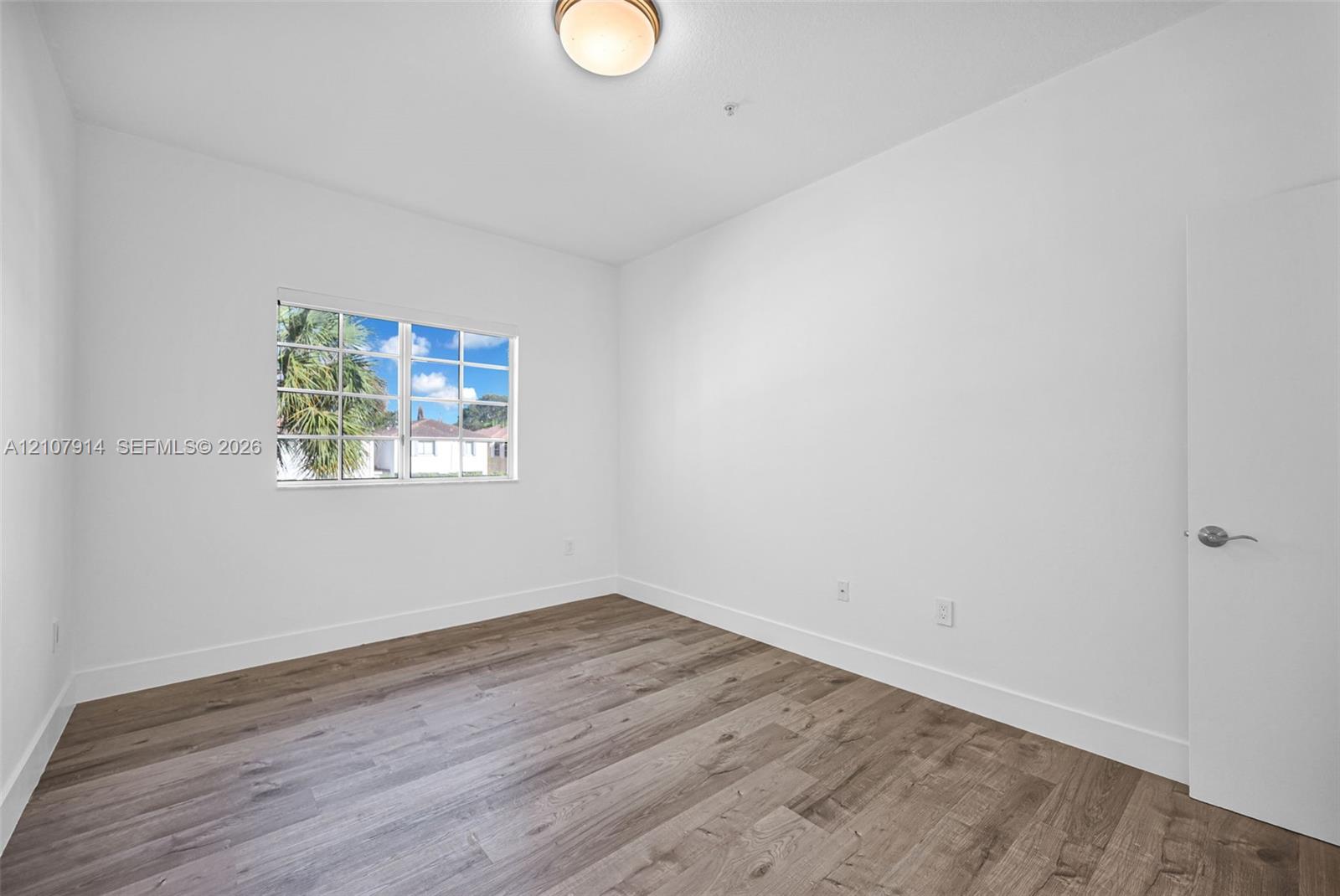 Room featuring wood-finish flooring, a multi-pane window, and a flush-mount ceiling fixture