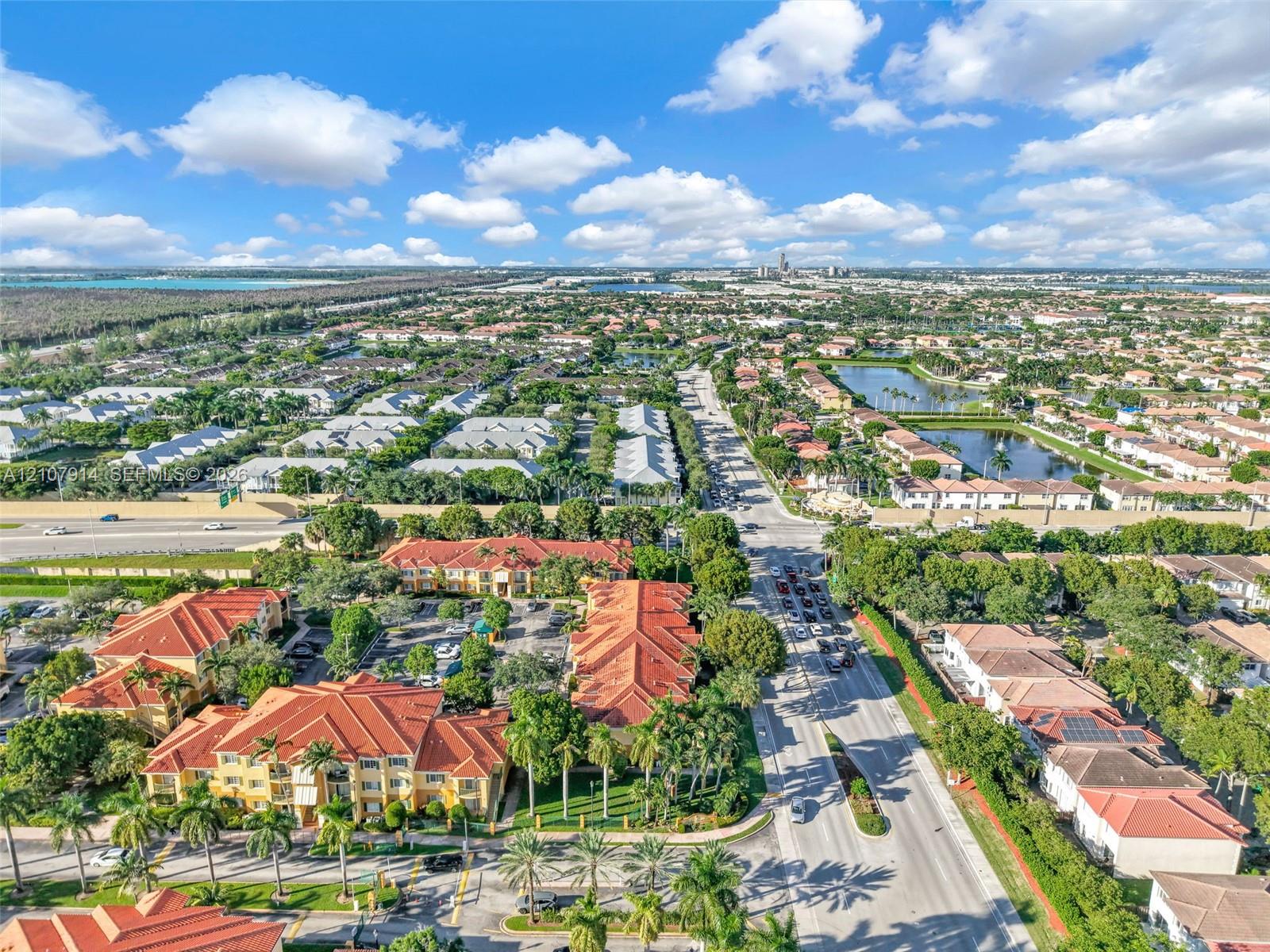 Aerial perspective of a multi-building residential complex featuring Mediterranean-style architecture, terracotta-tiled roofs, manicured palm landscaping, and integrated surface parking