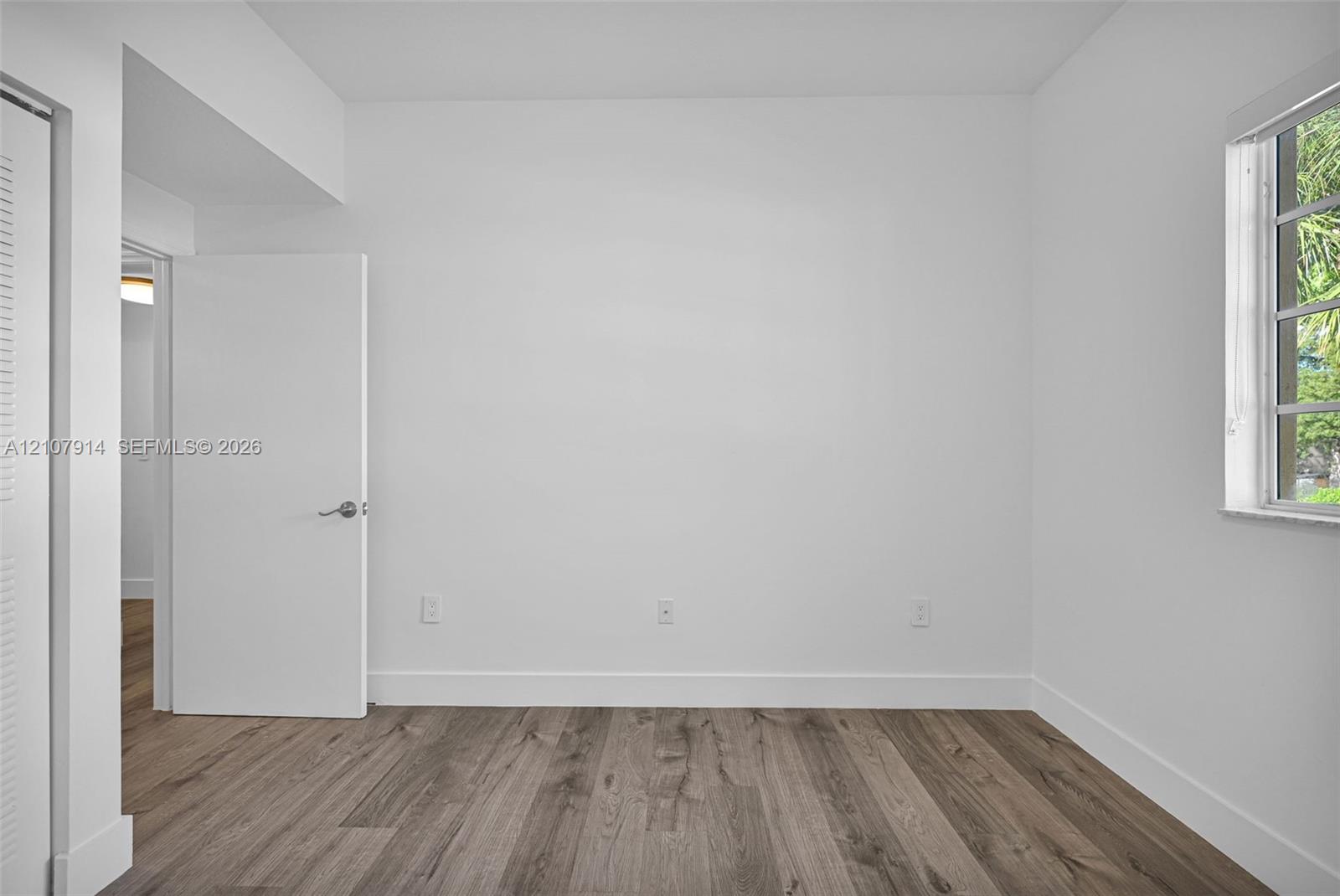 Interior space featuring wood-finish flooring, a multi-pane window, and white interior doors with brushed nickel hardware