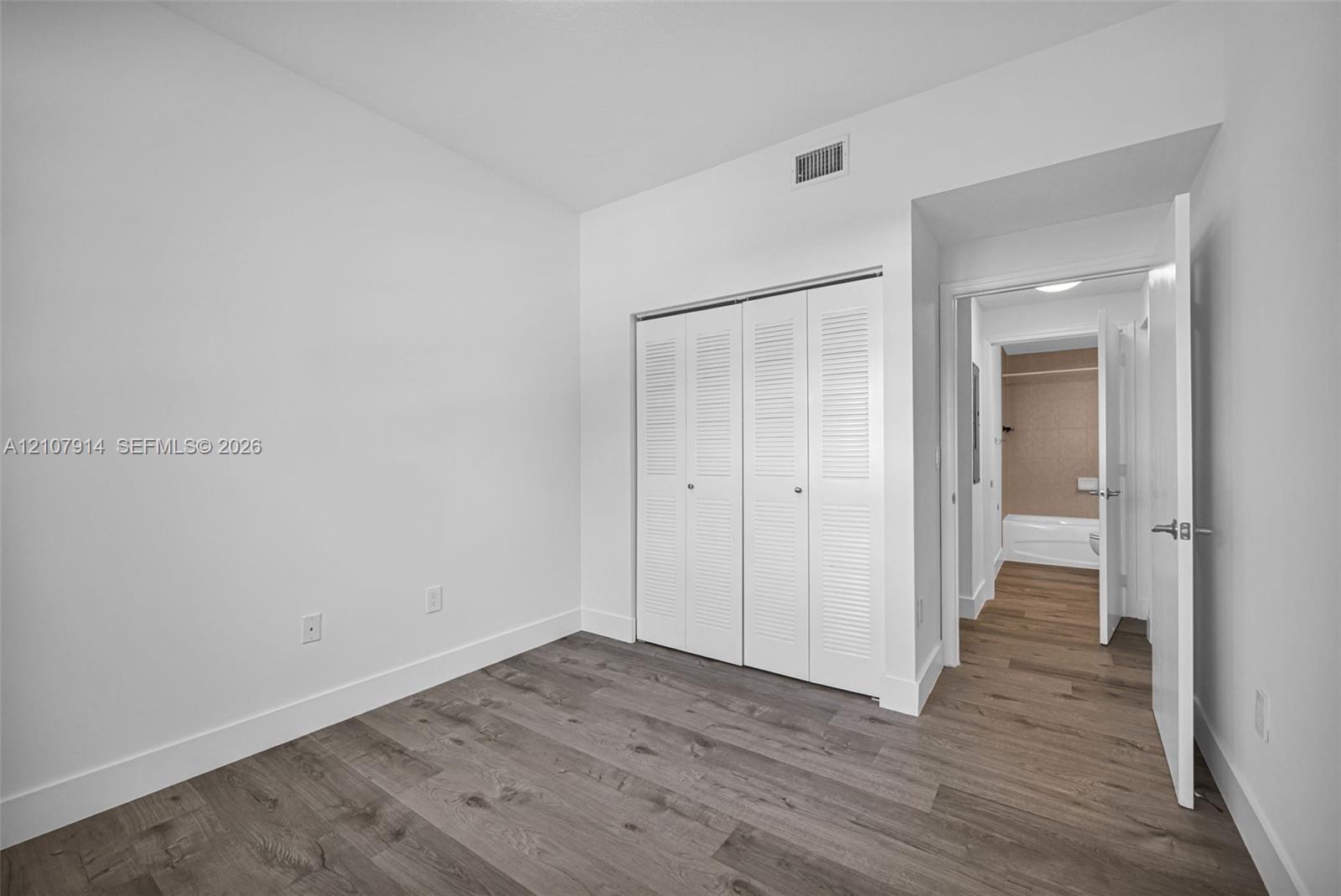 Room featuring wood-finish flooring, white walls, and a built-in double-door closet with louvered panels