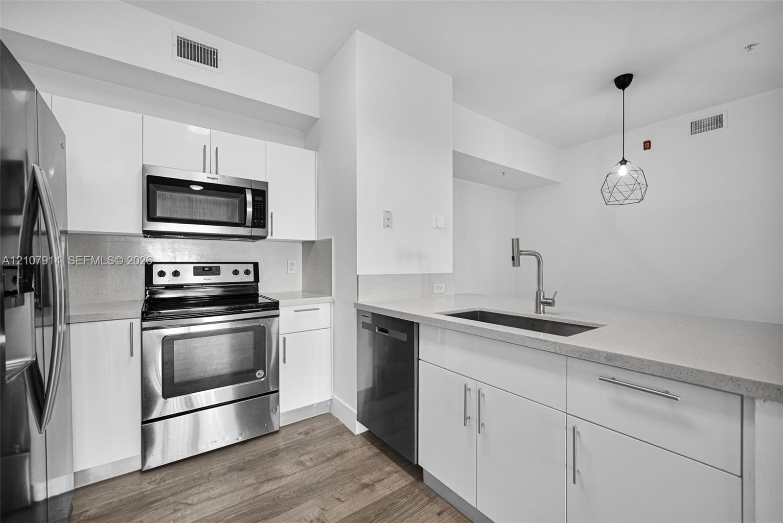 Kitchen featuring white cabinetry, solid surface countertops, stainless steel appliances, a single-basin undermount sink with a high-arch faucet, and wood-finish flooring