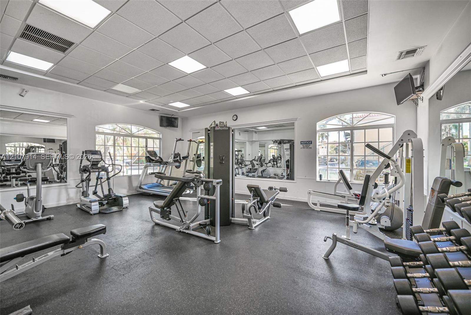 Fitness center featuring a drop ceiling with recessed panel lighting, rubberized flooring, and large wall-mounted mirrors