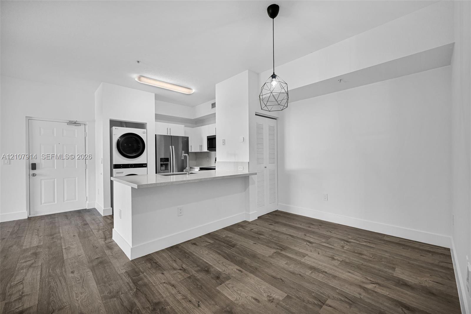 Kitchen featuring a breakfast bar with stone-surfaced countertop, stainless steel refrigerator, integrated laundry center, wood-finish flooring, and geometric pendant lighting