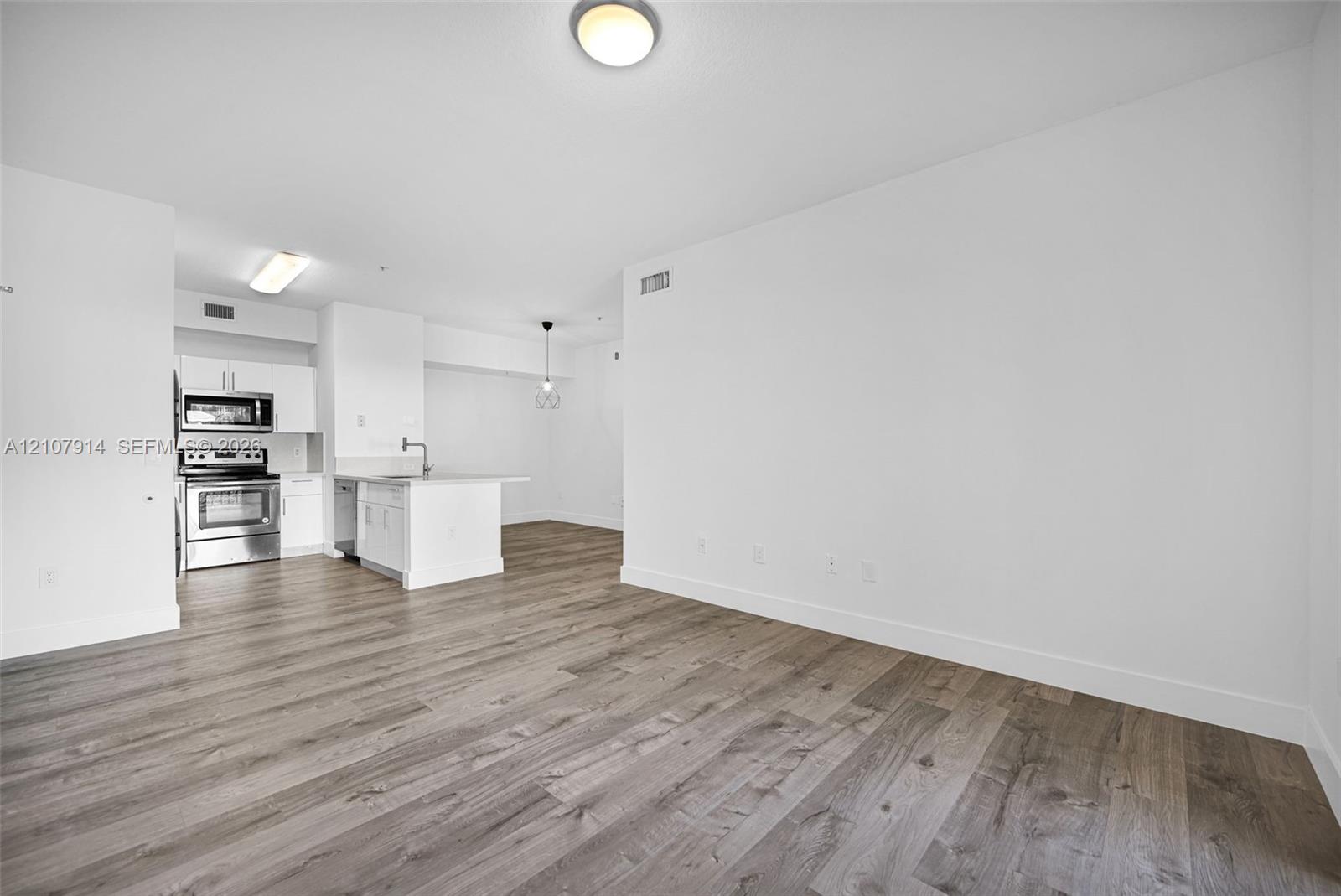 Open-concept interior featuring wood-finish flooring, white cabinetry, stainless steel appliances, and ceiling-mounted lighting fixtures