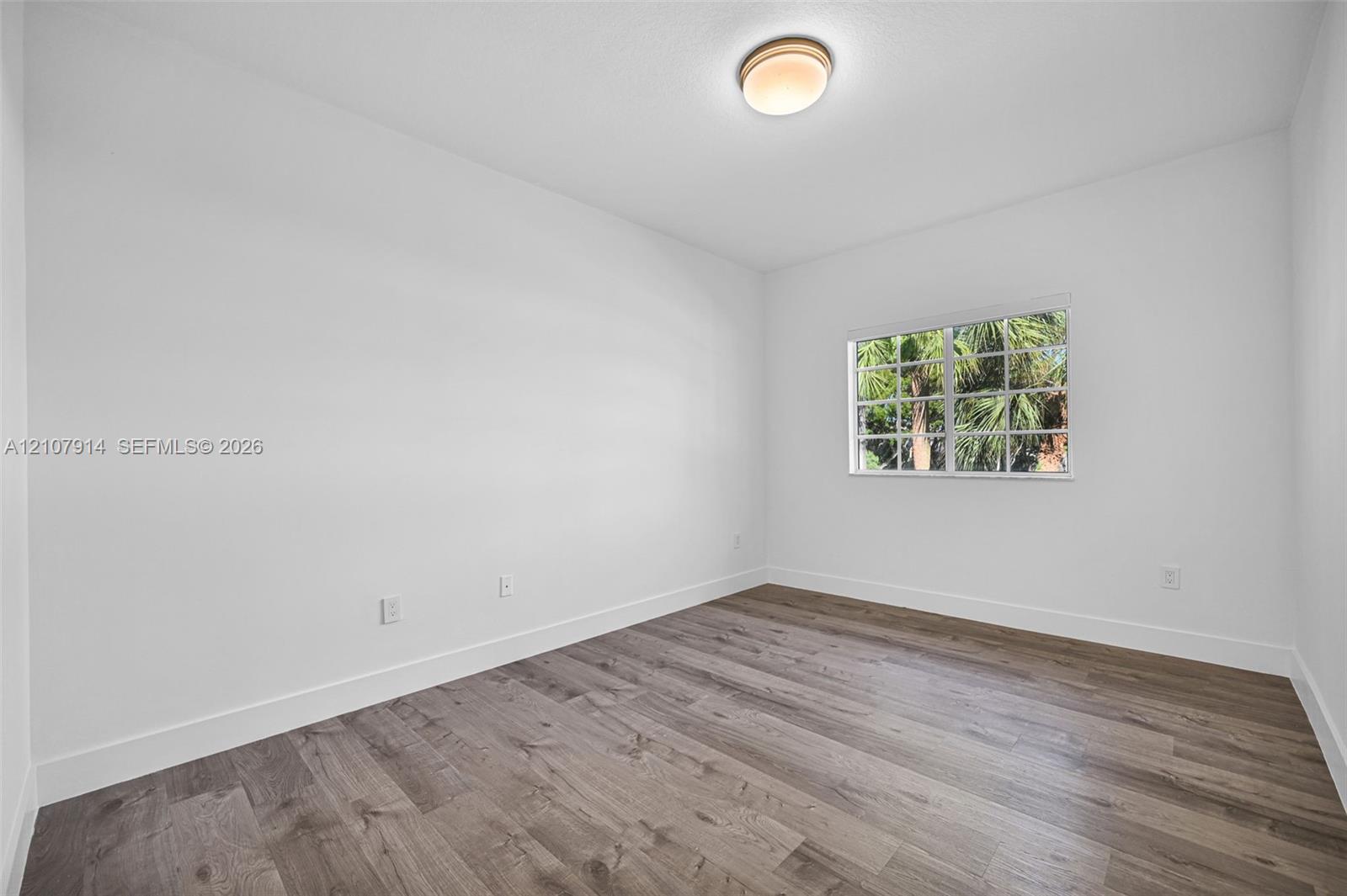 Neutral-toned room featuring wood-finish flooring, a multi-pane window, and a flush-mount dome light fixture