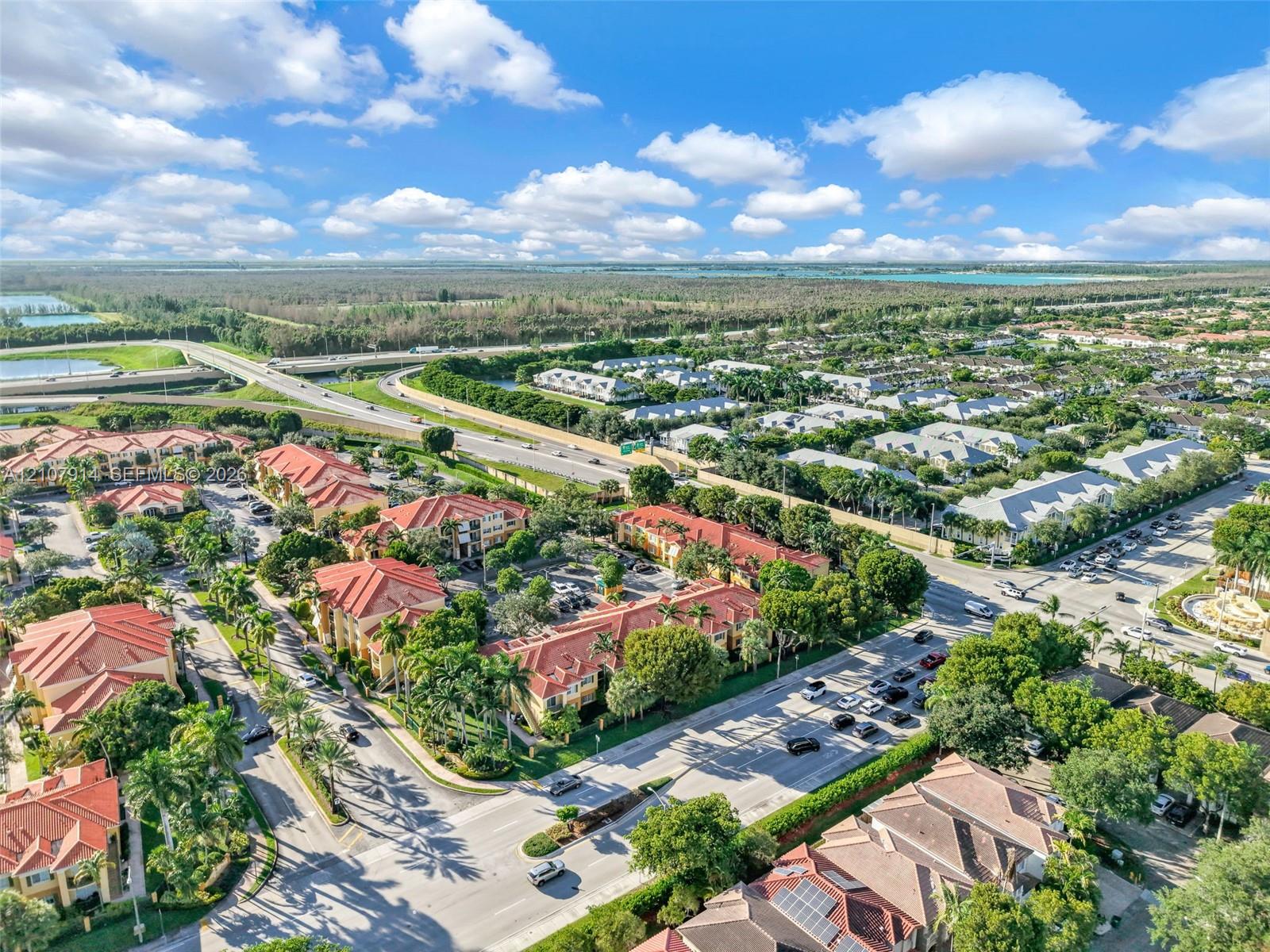Aerial perspective of a multi-building residential development featuring terracotta-style tile roofs, mature canopy trees, paved thoroughfares, and manicured landscaping