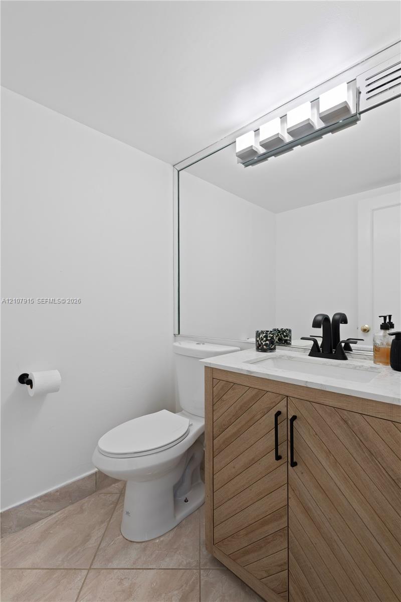 Vanity featuring wood-grain cabinet doors in a chevron pattern, light-toned stone countertop, integrated sink, matte black hardware, and an expansive wall-mounted mirror