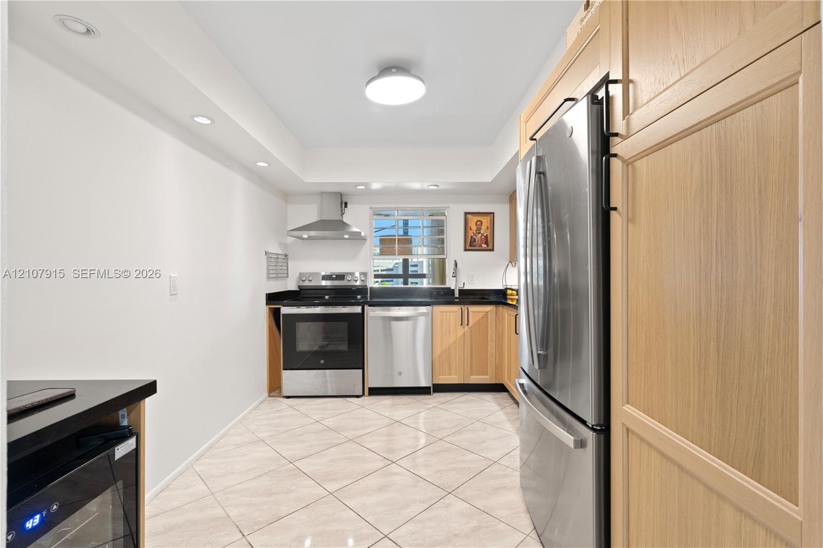 Kitchen featuring light-finish wood cabinetry, stainless steel appliances, dark stone countertops, tile flooring, and recessed ceiling lighting