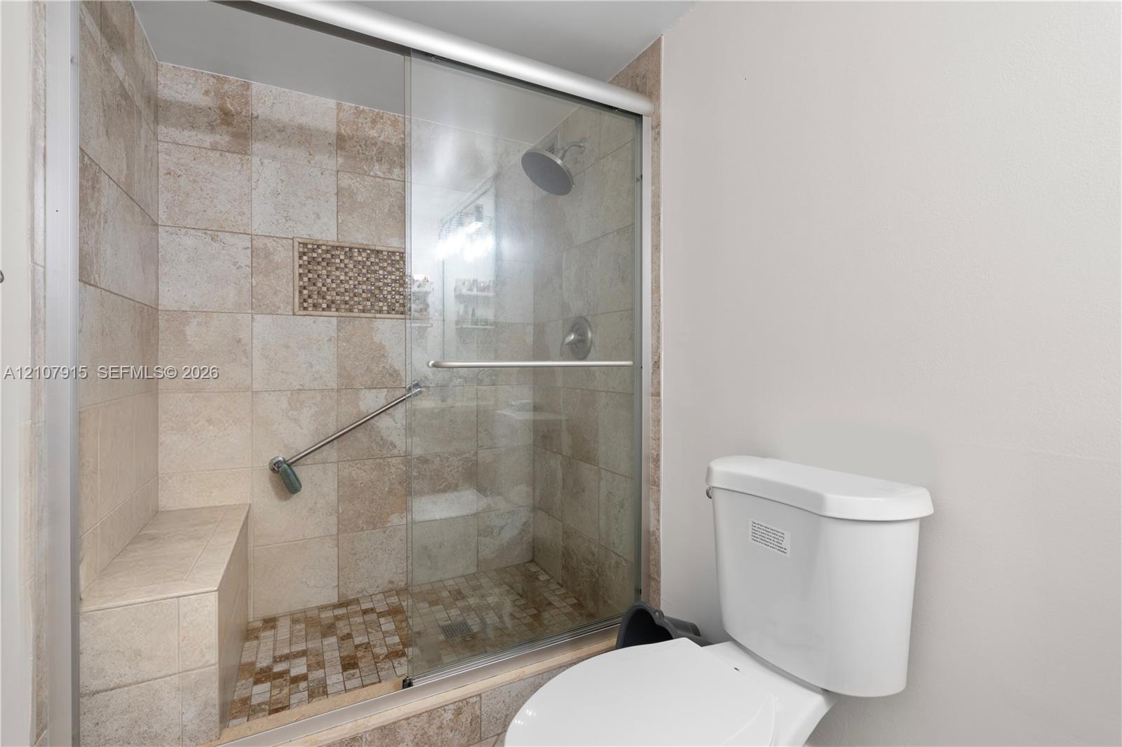 Walk-in shower featuring tile walls, a built-in bench, a decorative mosaic tile inset, a glass sliding door, and a wall-mounted shower head