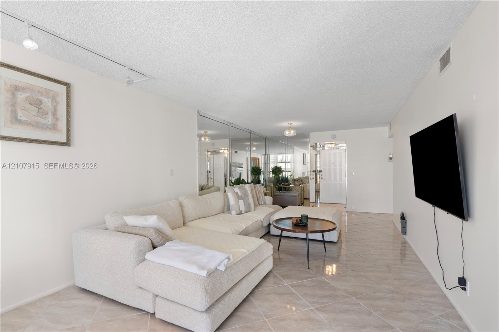 Neutral-toned interior space featuring diagonal-patterned ceramic tile flooring, full-wall mirrored paneling, and adjustable track lighting Neutral-toned interior space featuring diagonal-patterned ceramic tile flooring, full-wall mirrored paneling, and adjustable track lighting
