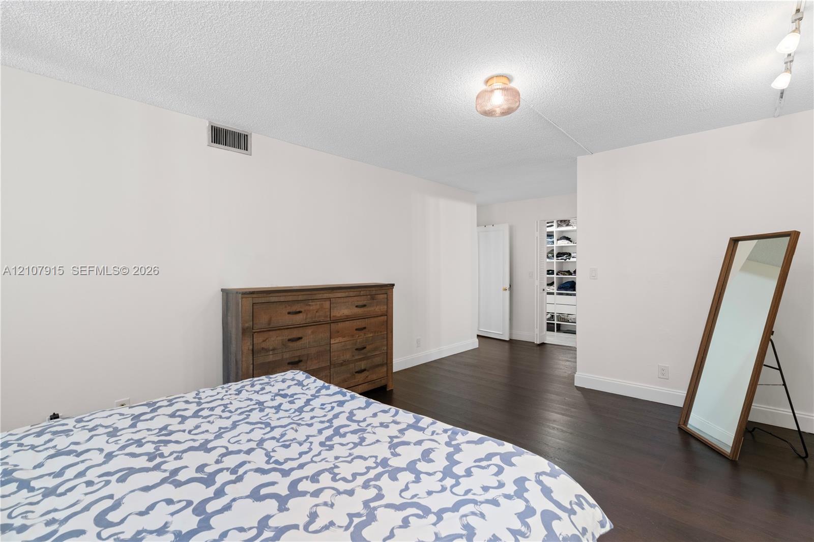 Dark wood-finish flooring and a walk-in closet featuring built-in shelving