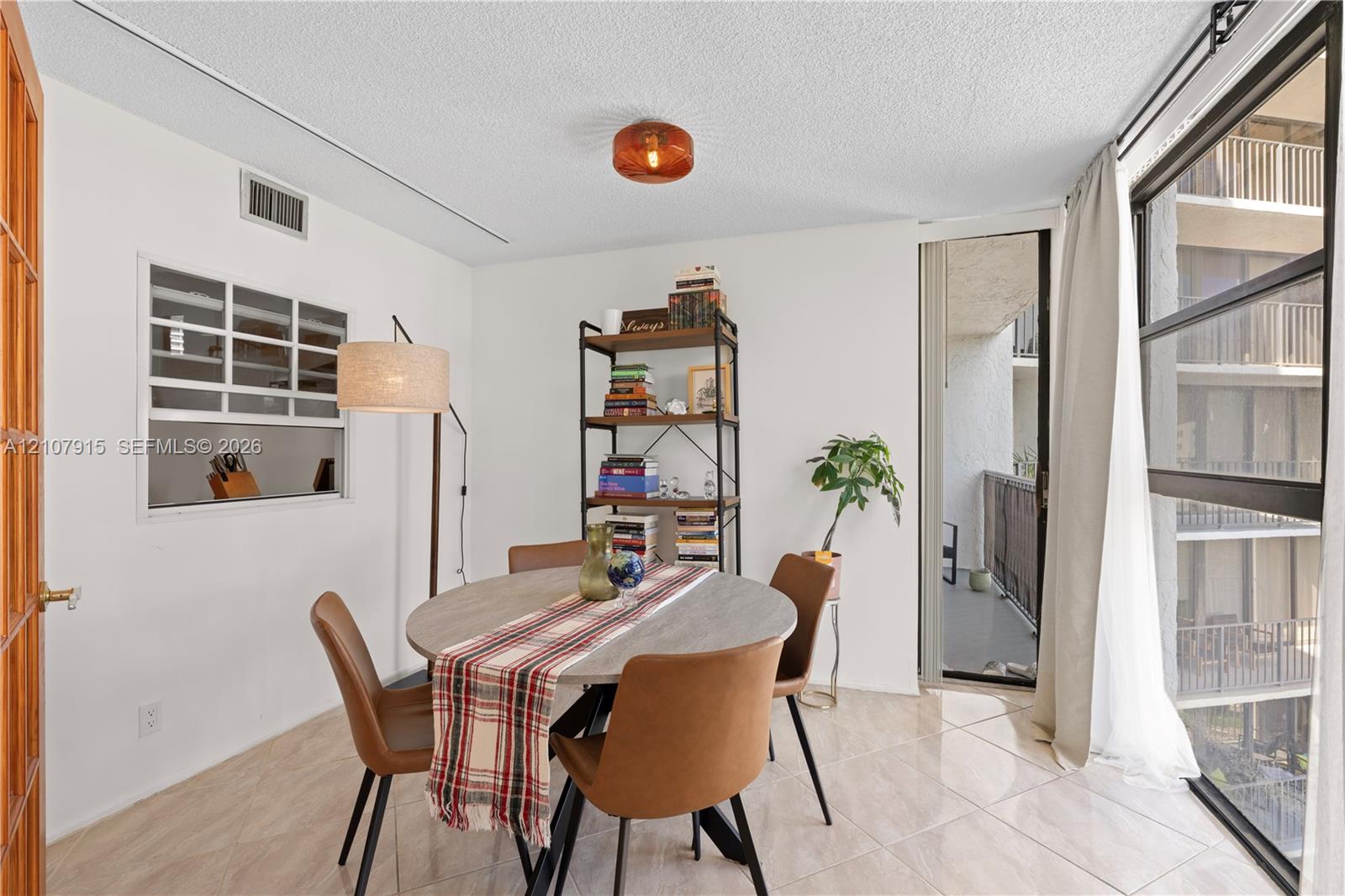Dining area featuring large-format ceramic tile flooring, a built-in kitchen pass-through window, and floor-to-ceiling windows with sliding door access to a private balcony