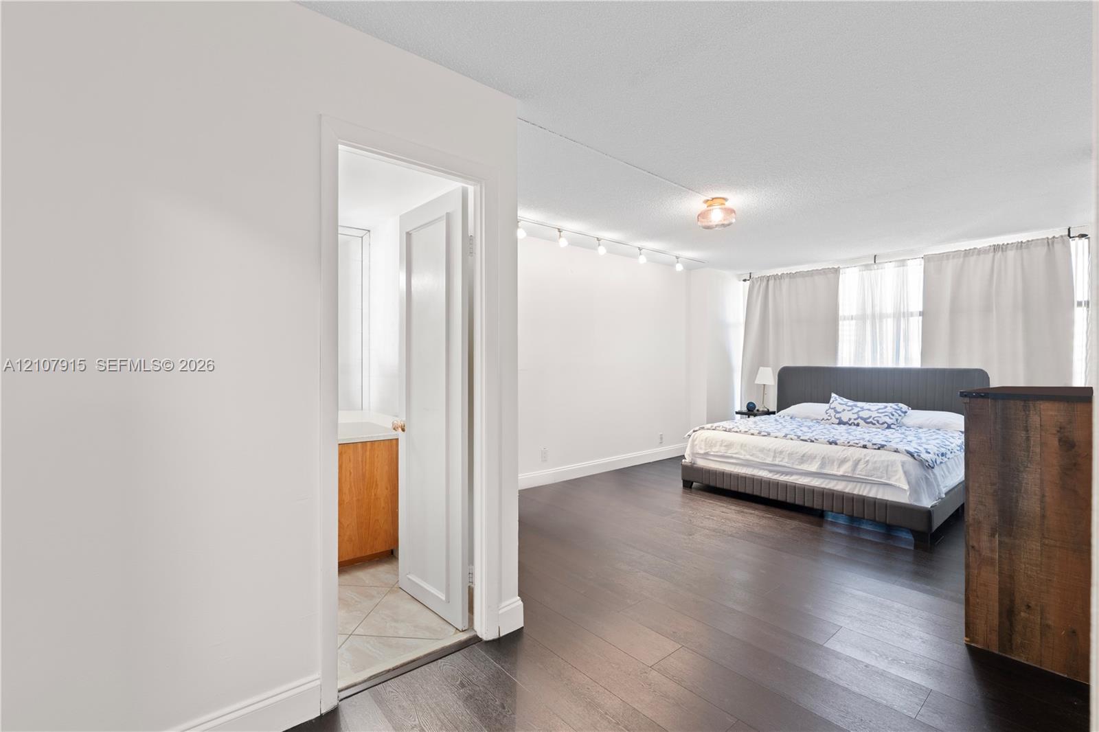 Dark wood-finish flooring, adjustable track lighting, and a bathroom featuring tile flooring and a light-finish wood vanity