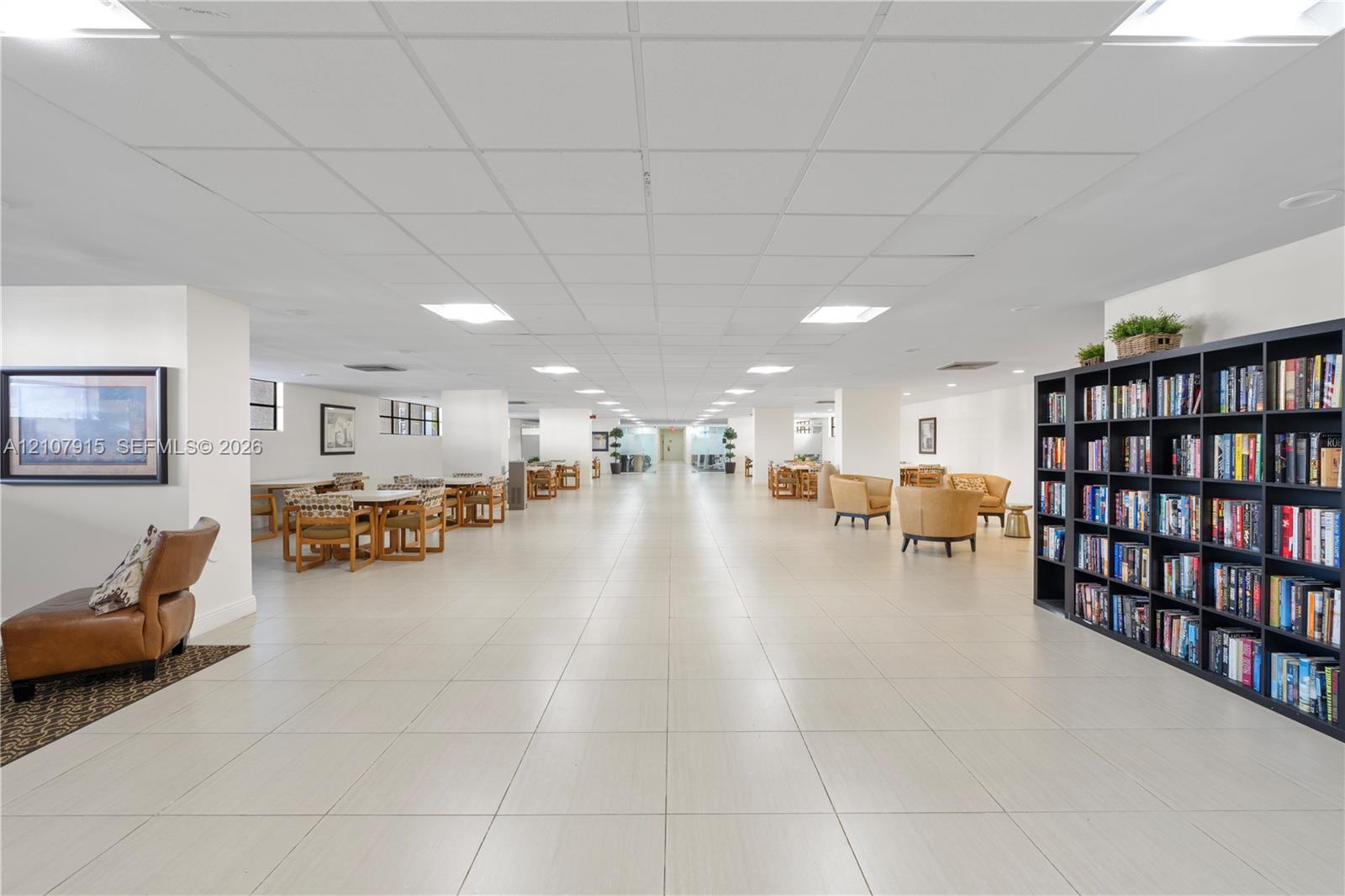 Expansive common area featuring large-format tile flooring, a suspended grid ceiling with recessed panel lighting, and a floor-to-ceiling built-in bookcase