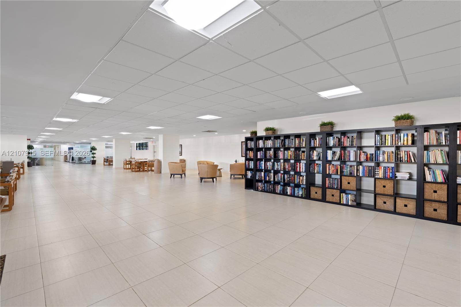 Expansive open-concept space featuring large-format tile flooring, recessed grid ceiling, integrated square lighting panels, and extensive floor-to-ceiling built-in shelving