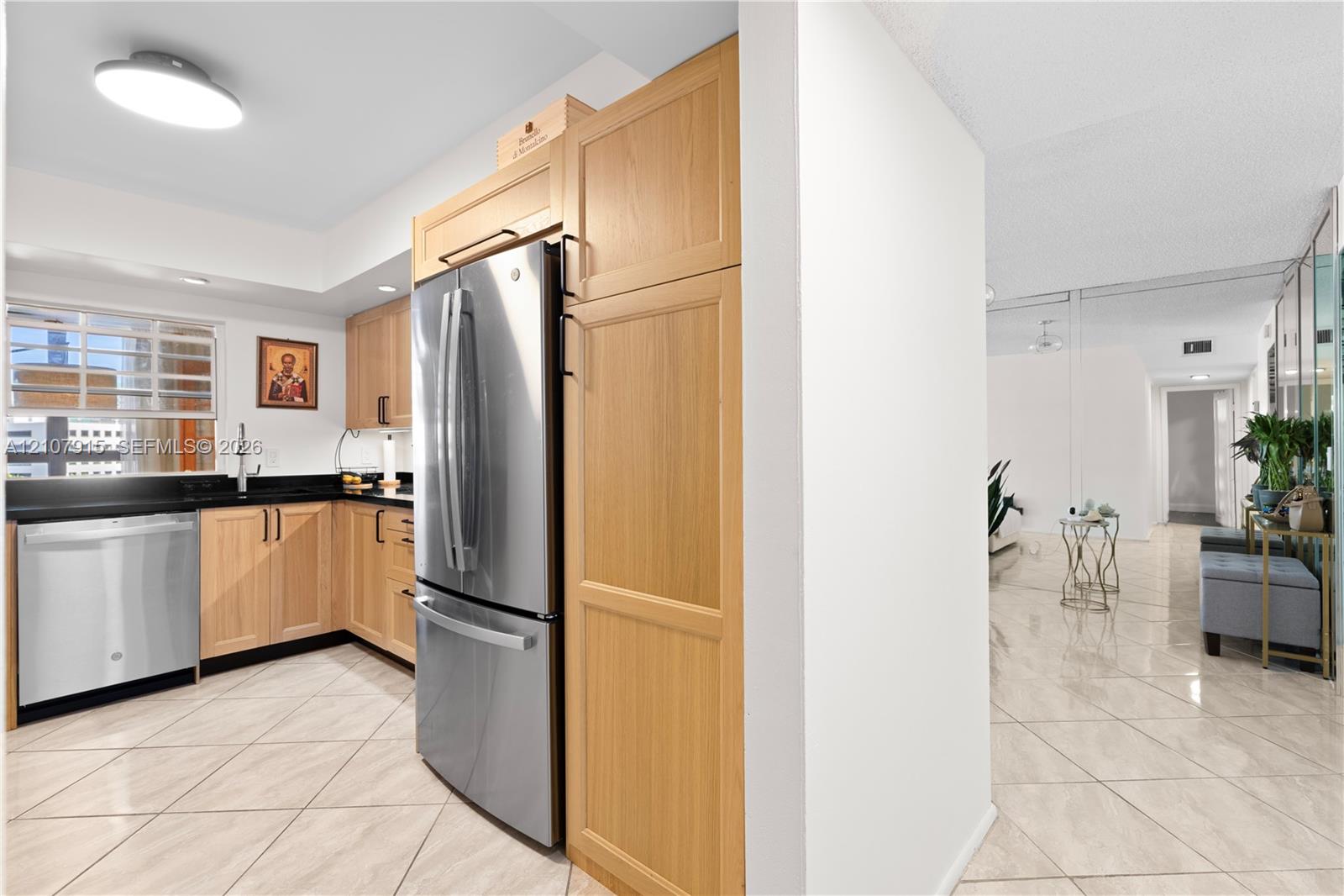 Kitchen featuring natural wood cabinetry, stainless steel appliances, dark stone countertops, and light-toned tile flooring