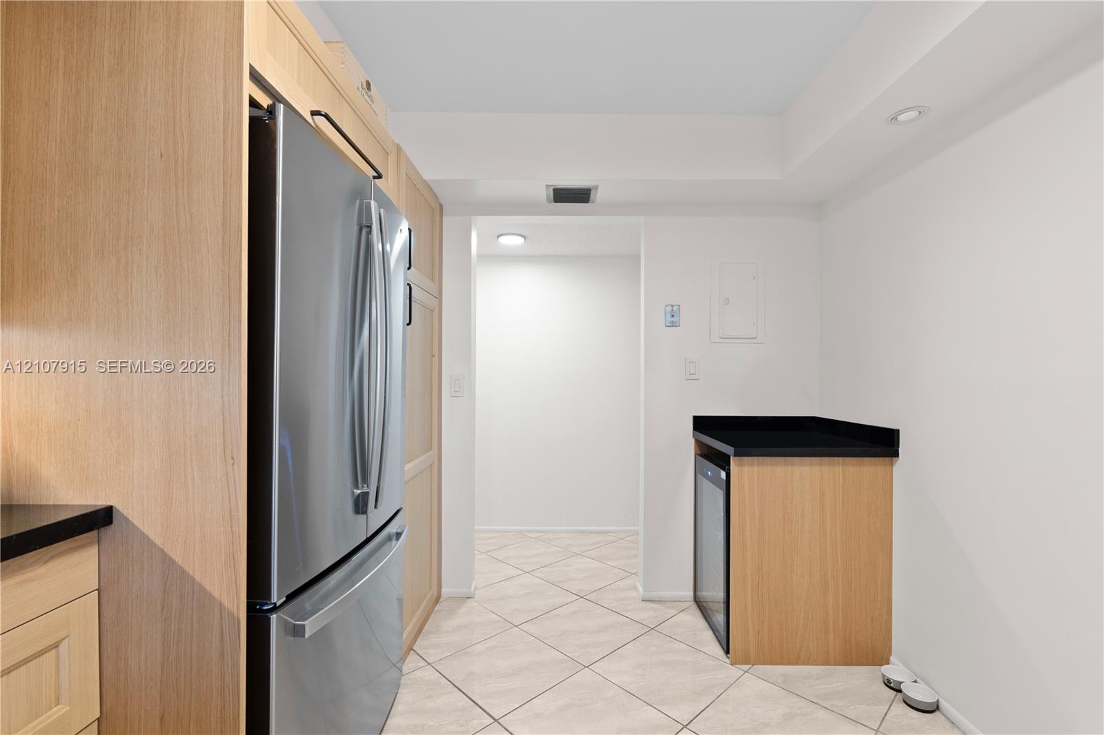 Kitchen featuring light wood-finish cabinetry, stainless steel French door refrigerator, black countertops, and beverage refrigerator