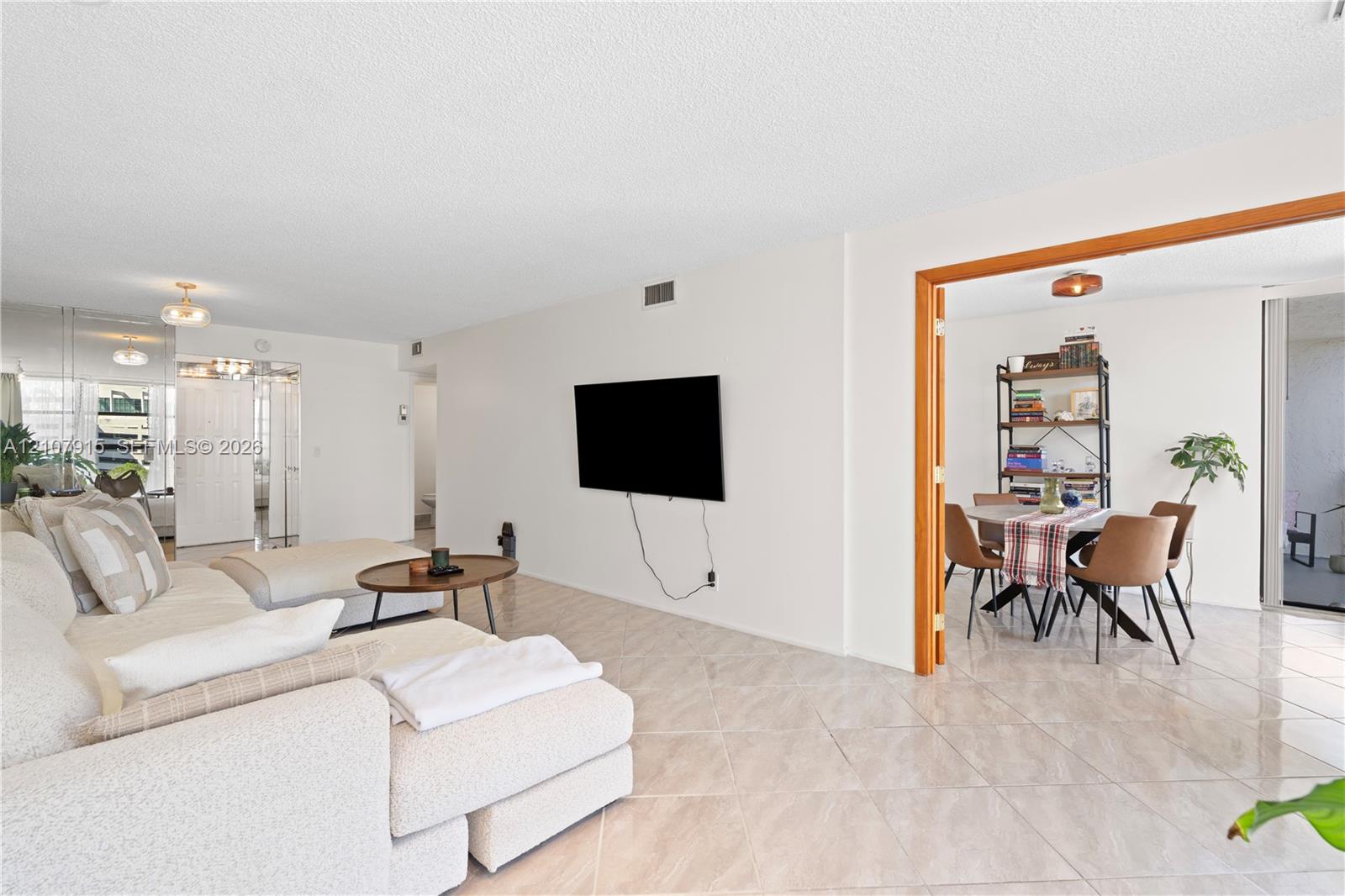 Open-concept interior featuring light-toned tile flooring, neutral wall finishes, and a wide interior doorway framed with wood trim Open-concept interior featuring light-toned tile flooring, neutral wall finishes, and a wide interior doorway framed with wood trim
