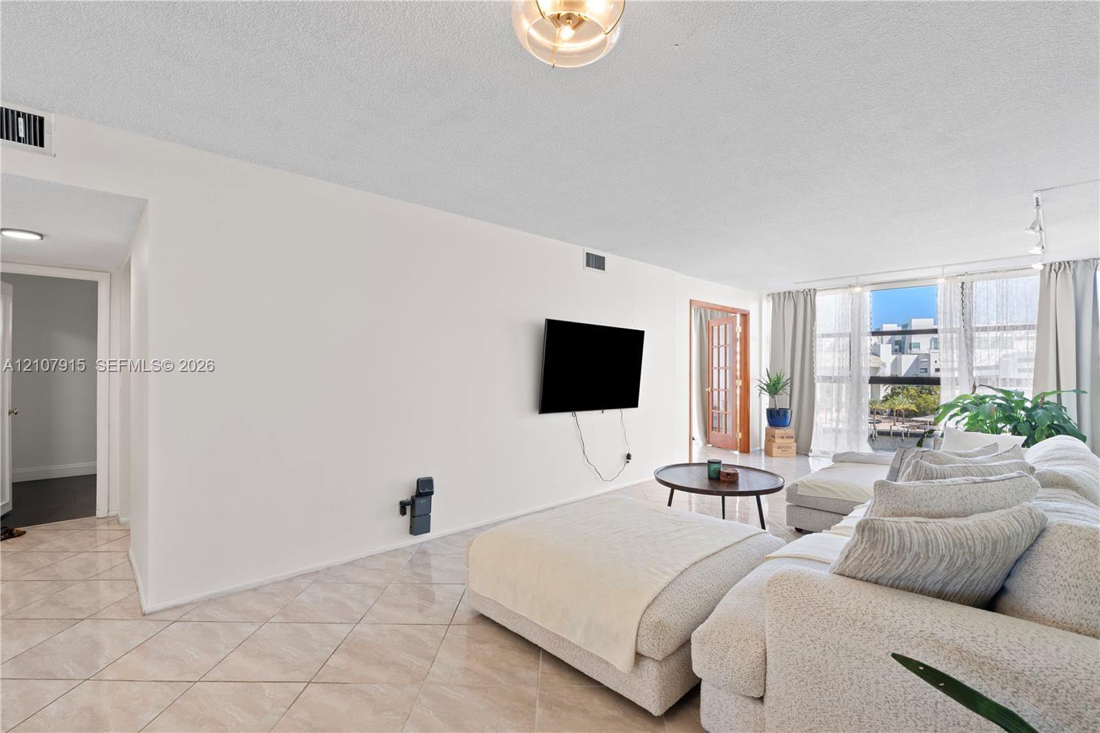 Open-concept room featuring light-colored tile flooring set on a diagonal, floor-to-ceiling windows, and wood-framed glass pane interior doors Open-concept room featuring light-colored tile flooring set on a diagonal, floor-to-ceiling windows, and wood-framed glass pane interior doors