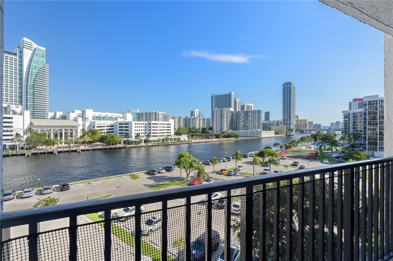 Covered private balcony featuring black metal railings and direct water and urban skyline scenery