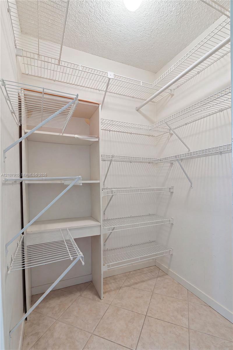 Storage area featuring built-in vertical shelving, multi-level wire rack organizers, and tile flooring