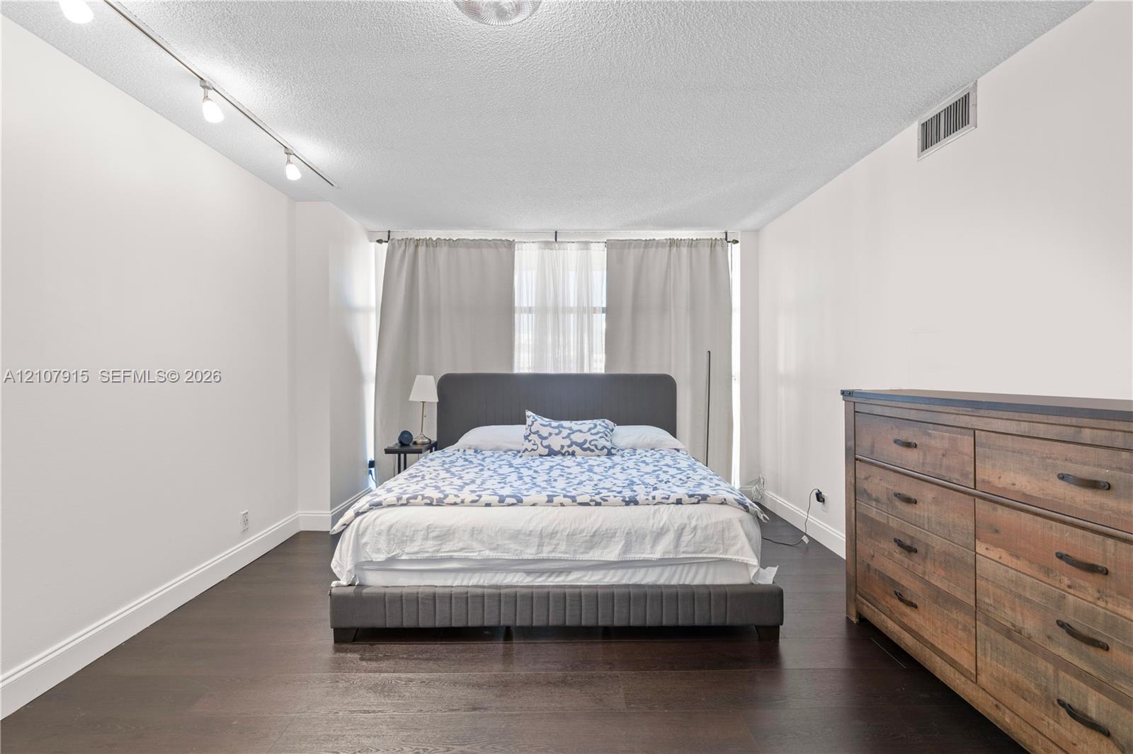 Spacious interior featuring dark wood-finish flooring, adjustable track lighting, and expansive window coverage with full-length drapery