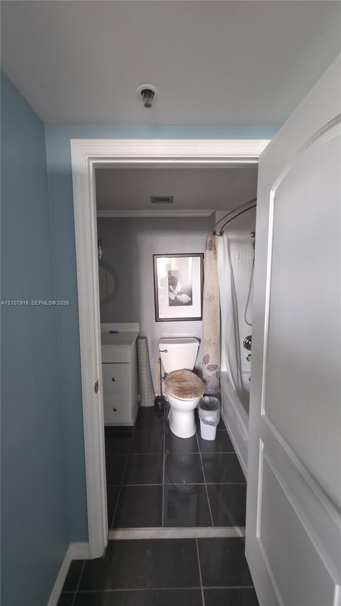 Bathroom featuring dark tile flooring, a white cabinet vanity, and a shower-tub combination with a curved shower rod