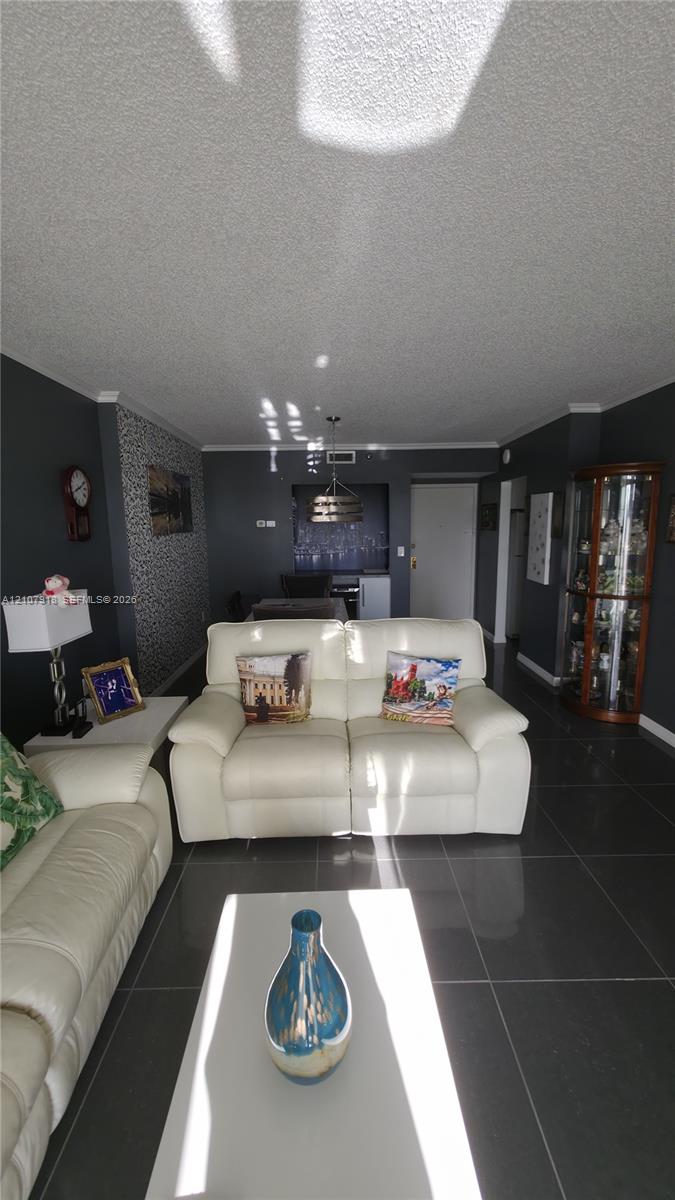Living area featuring large-format dark tile flooring, a textured accent wall, crown molding, and a suspended metal pendant light fixture Living area featuring large-format dark tile flooring, a textured accent wall, crown molding, and a suspended metal pendant light fixture