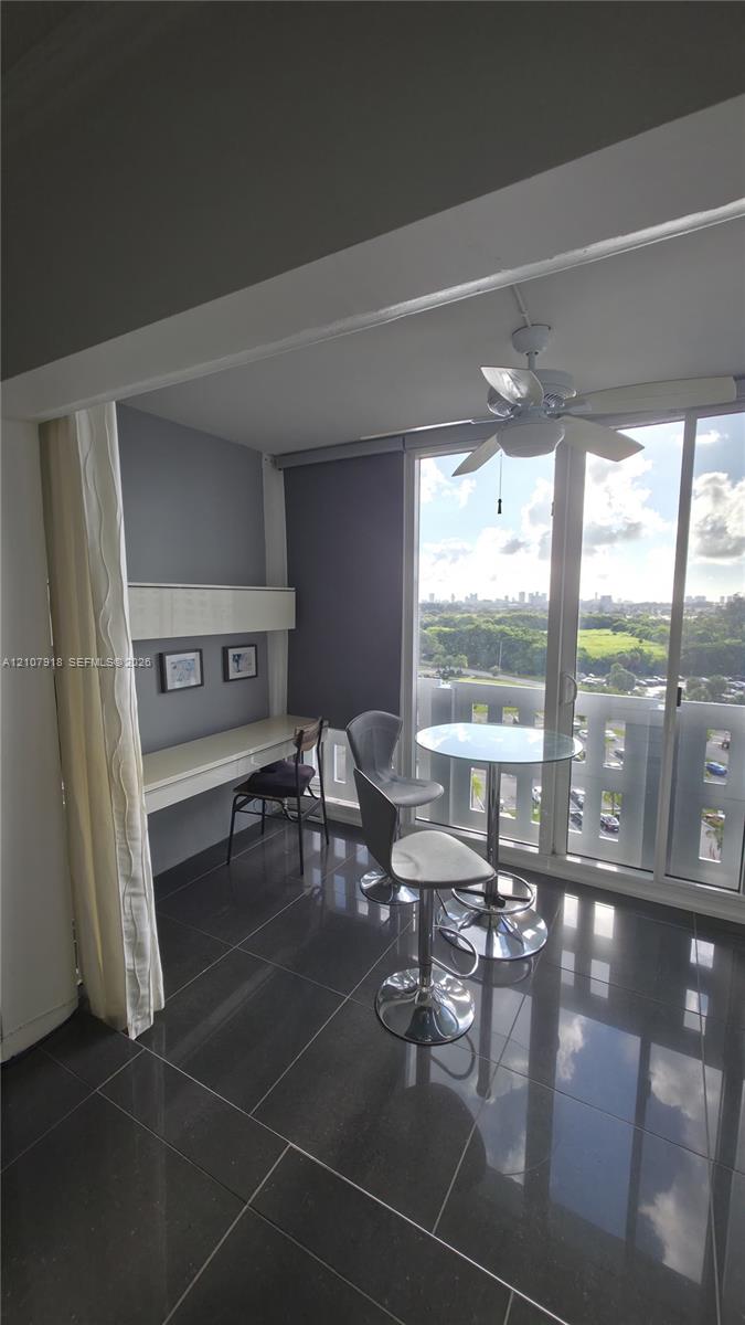 Floor-to-ceiling windows with expansive exterior scenery, integrated wall-mounted desk with overhead storage, polished tile flooring, and ceiling fan