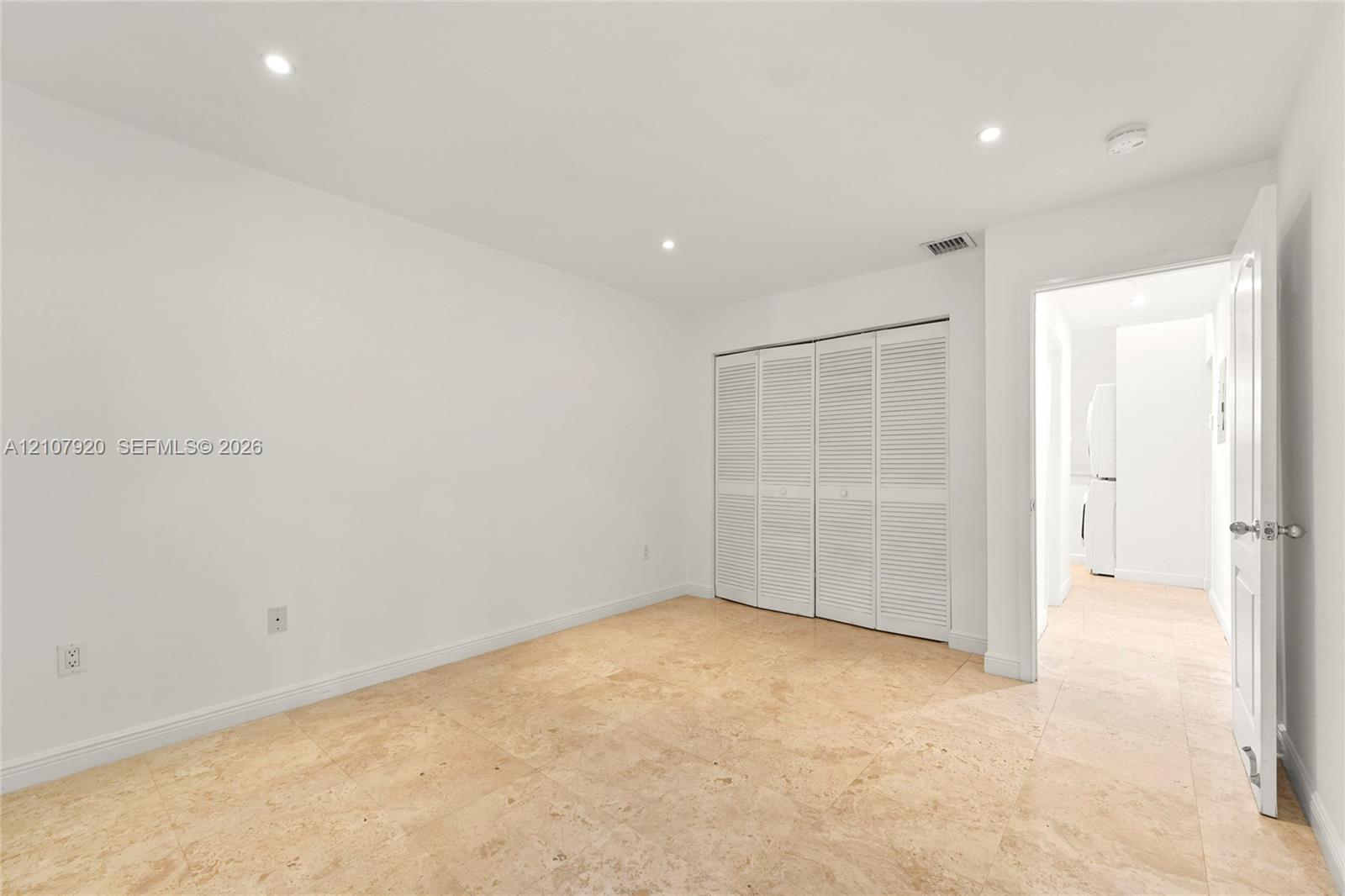 Neutral-toned stone flooring, recessed ceiling lighting, and a multi-panel closet with louvered doors