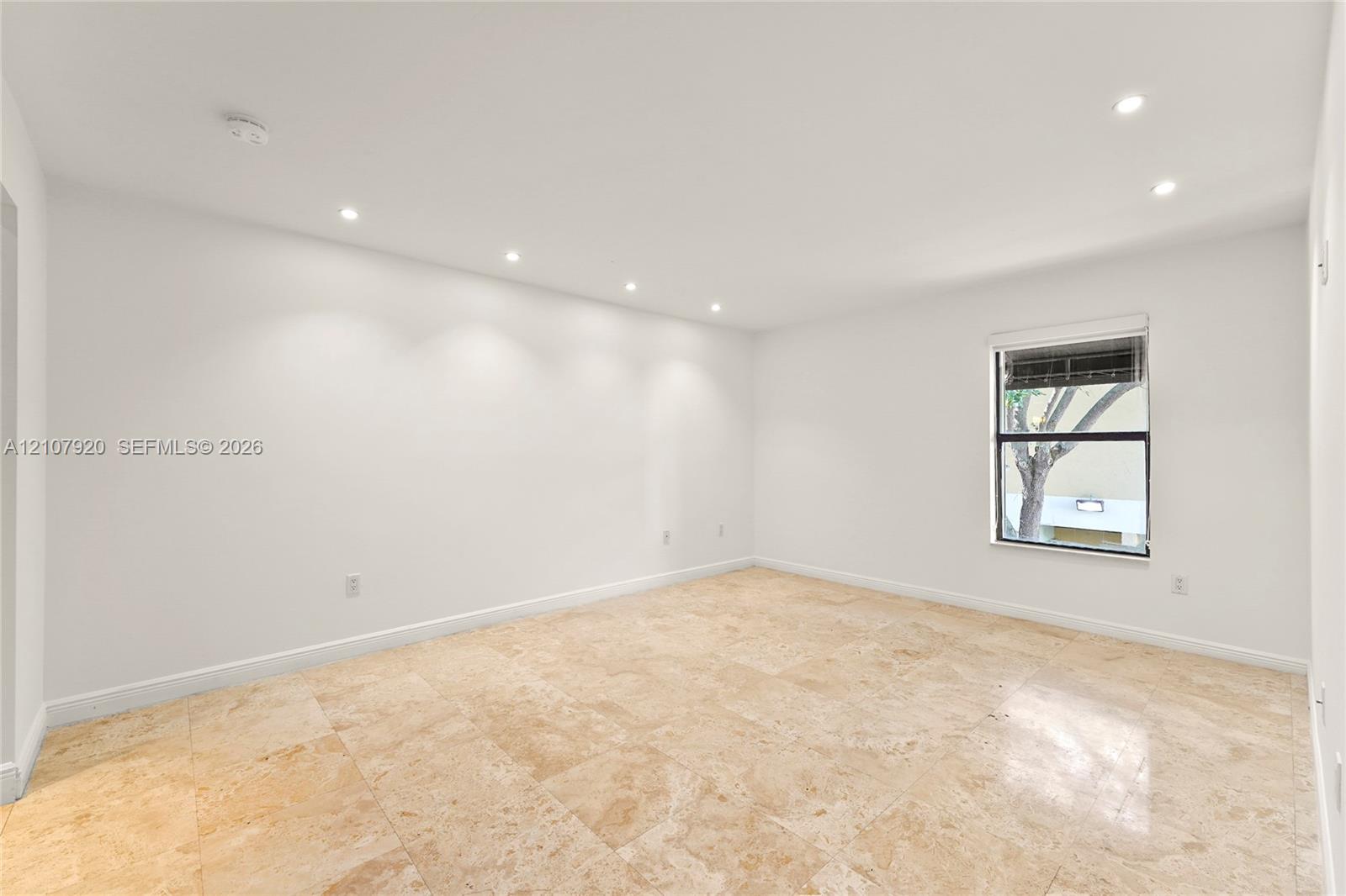 Interior space featuring large-format stone flooring, recessed ceiling lighting, and a single-pane window with integrated blinds