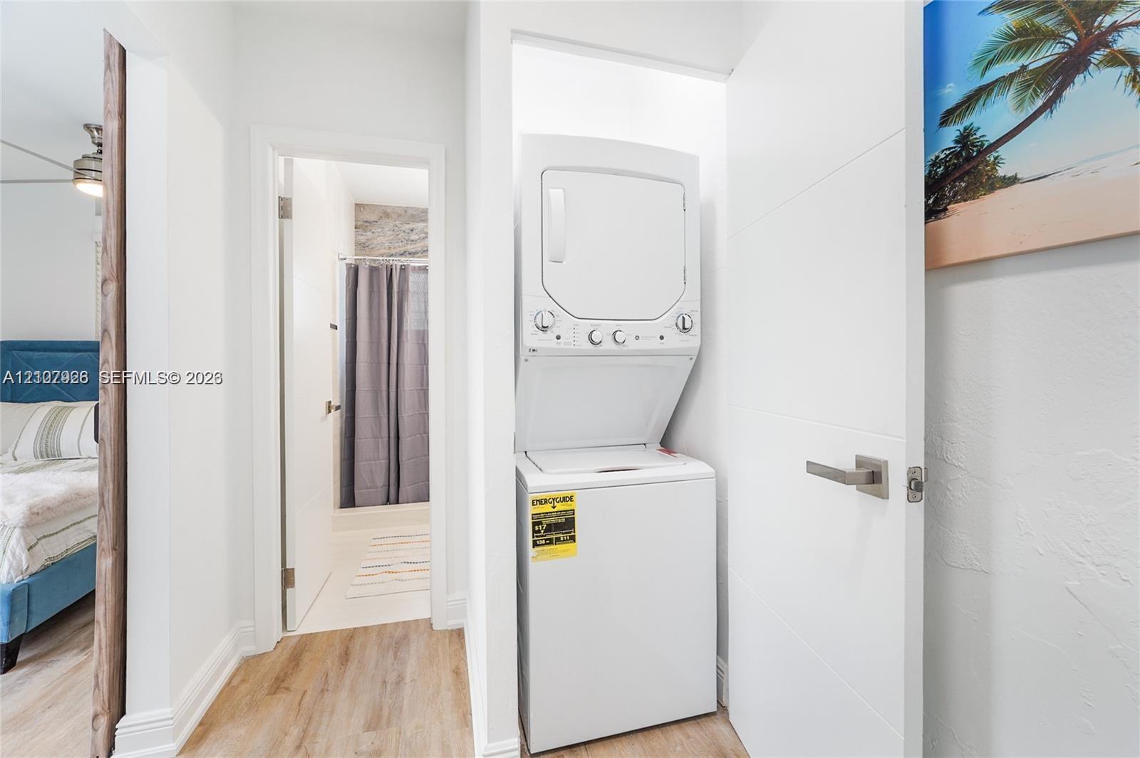 Stacked laundry unit housed within a built-in closet, featuring neutral walls, wood-finish flooring, and a sleek paneled door with satin-finish hardware
