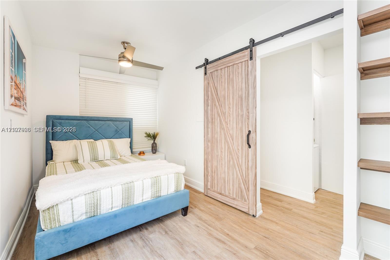 Wood-finish flooring, sliding barn door with black hardware, built-in wooden shelving, and ceiling-mounted light fixture