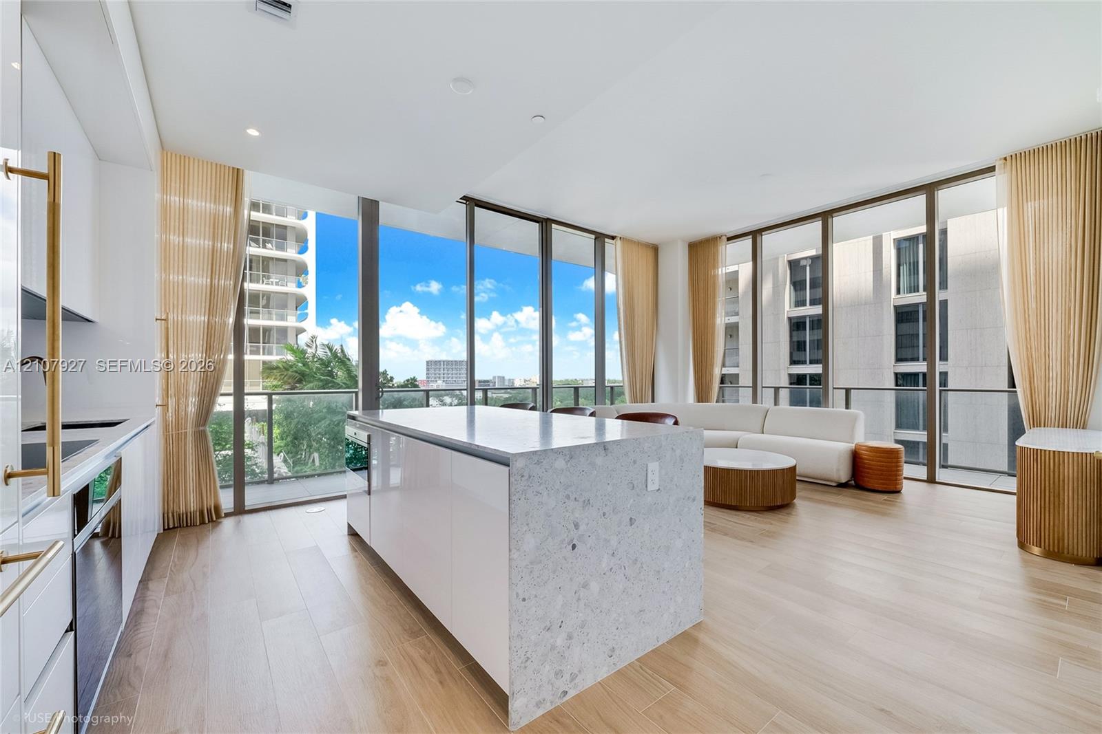 Kitchen featuring a central island with a stone-finish countertop, high-gloss cabinetry, floor-to-ceiling glass windows, and wood-finish flooring Kitchen featuring a central island with a stone-finish countertop, high-gloss cabinetry, floor-to-ceiling glass windows, and wood-finish flooring