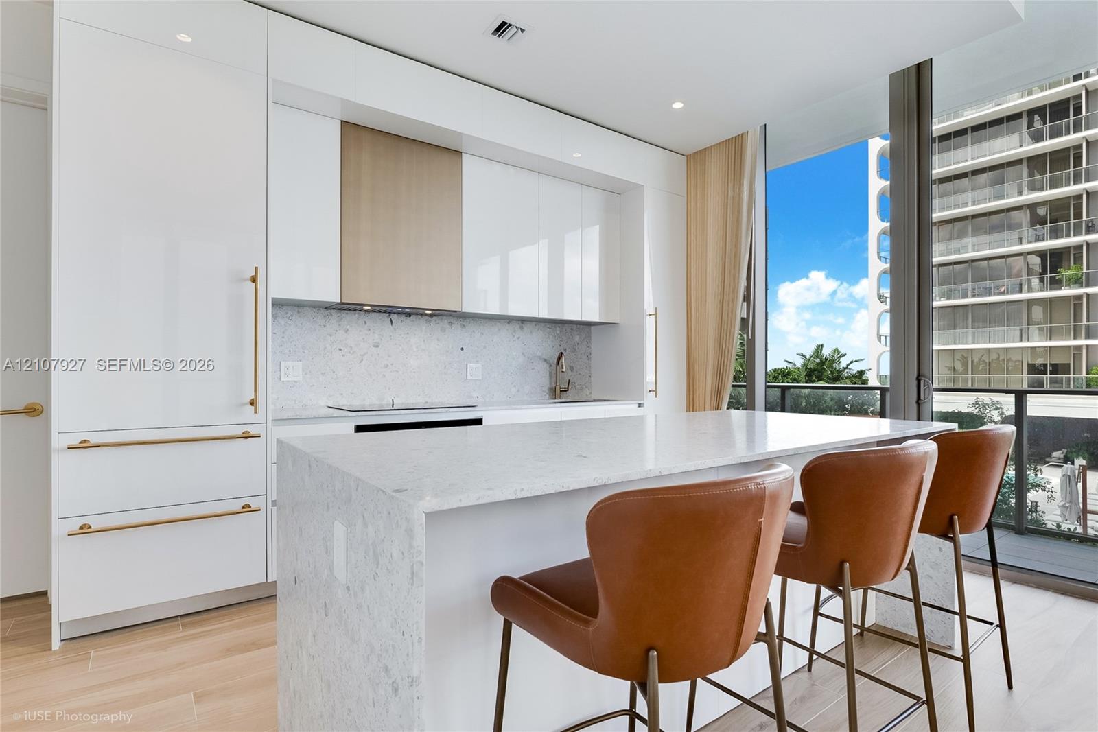 Modern kitchen featuring high-gloss cabinetry, a stone-surfaced waterfall island, integrated appliances, and wood-finish flooring Modern kitchen featuring high-gloss cabinetry, a stone-surfaced waterfall island, integrated appliances, and wood-finish flooring