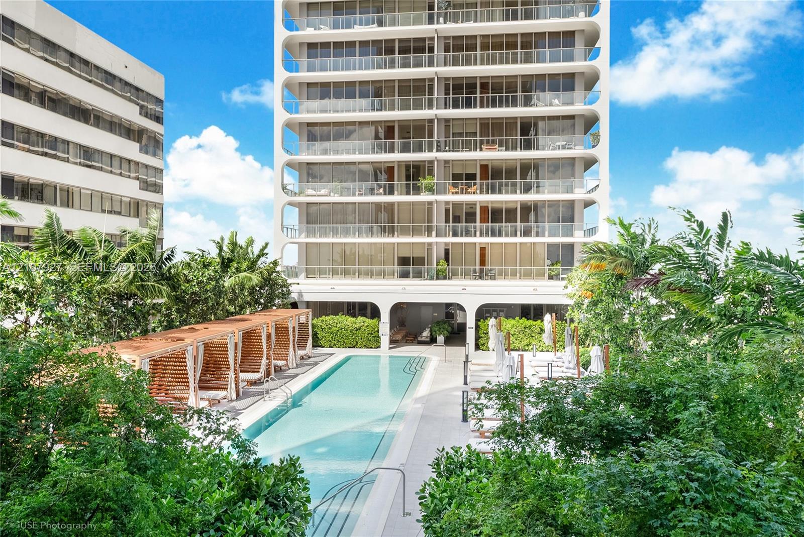 High-rise building exterior with wraparound balconies, rectangular swimming pool, integrated poolside cabanas, and mature perimeter landscaping High-rise building exterior with wraparound balconies, rectangular swimming pool, integrated poolside cabanas, and mature perimeter landscaping