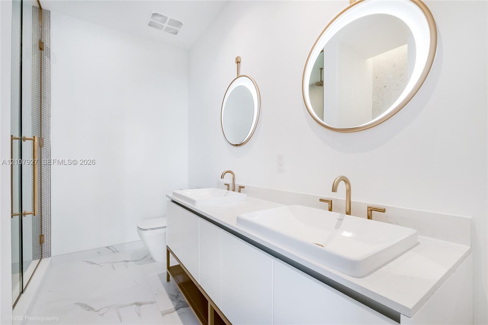Dual-sink vanity featuring stone-composite countertops, integrated vessel sinks, and brass-tone hardware
