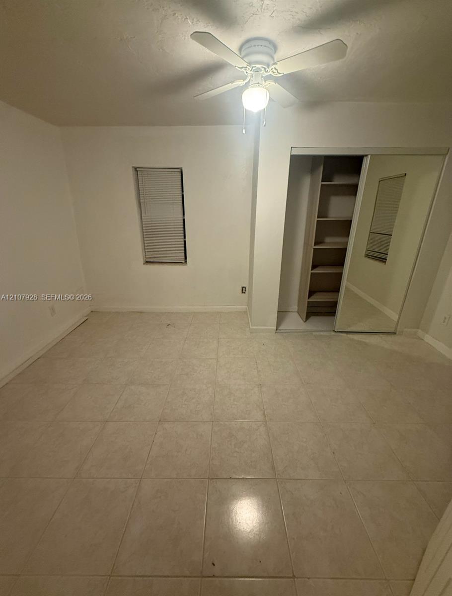 Neutral tile flooring, ceiling fan with integrated lighting, recessed window, closet with built-in shelving, and mirrored sliding closet doors