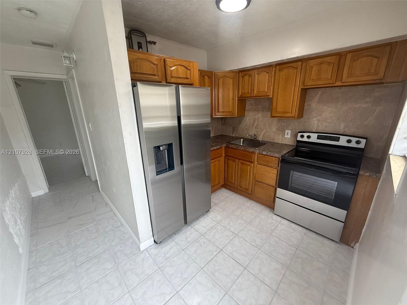 Kitchen featuring wood cabinetry, stainless steel side-by-side refrigerator, stainless steel electric range, stone-patterned backsplash, and ceramic tile flooring