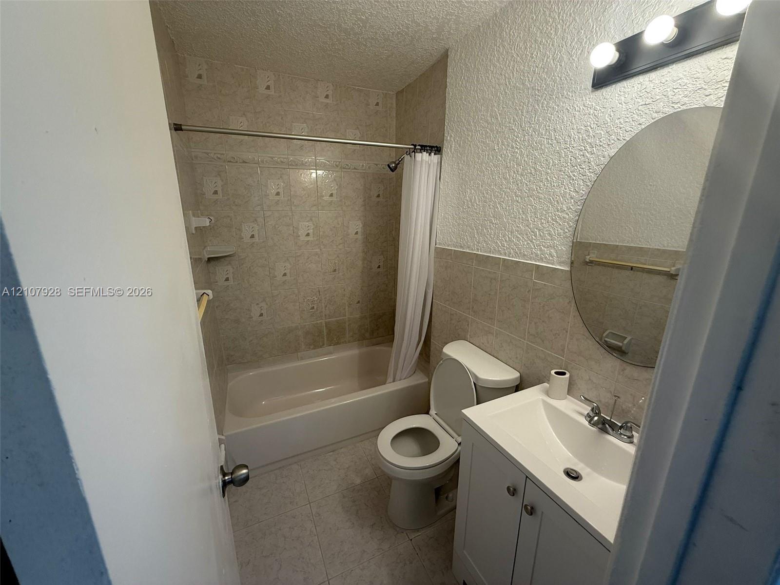 Bathroom featuring a vanity with integrated sink, oval wall-mounted mirror, three-light fixture, tile wainscoting, and a tiled tub and shower combination