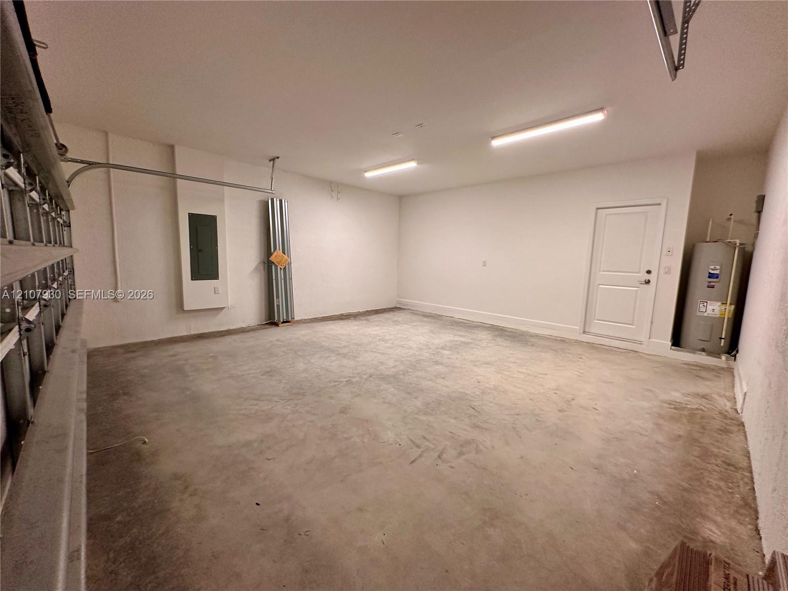 Multi-car garage featuring a concrete floor, dual linear overhead light fixtures, a paneled interior access door, and an integrated water heater