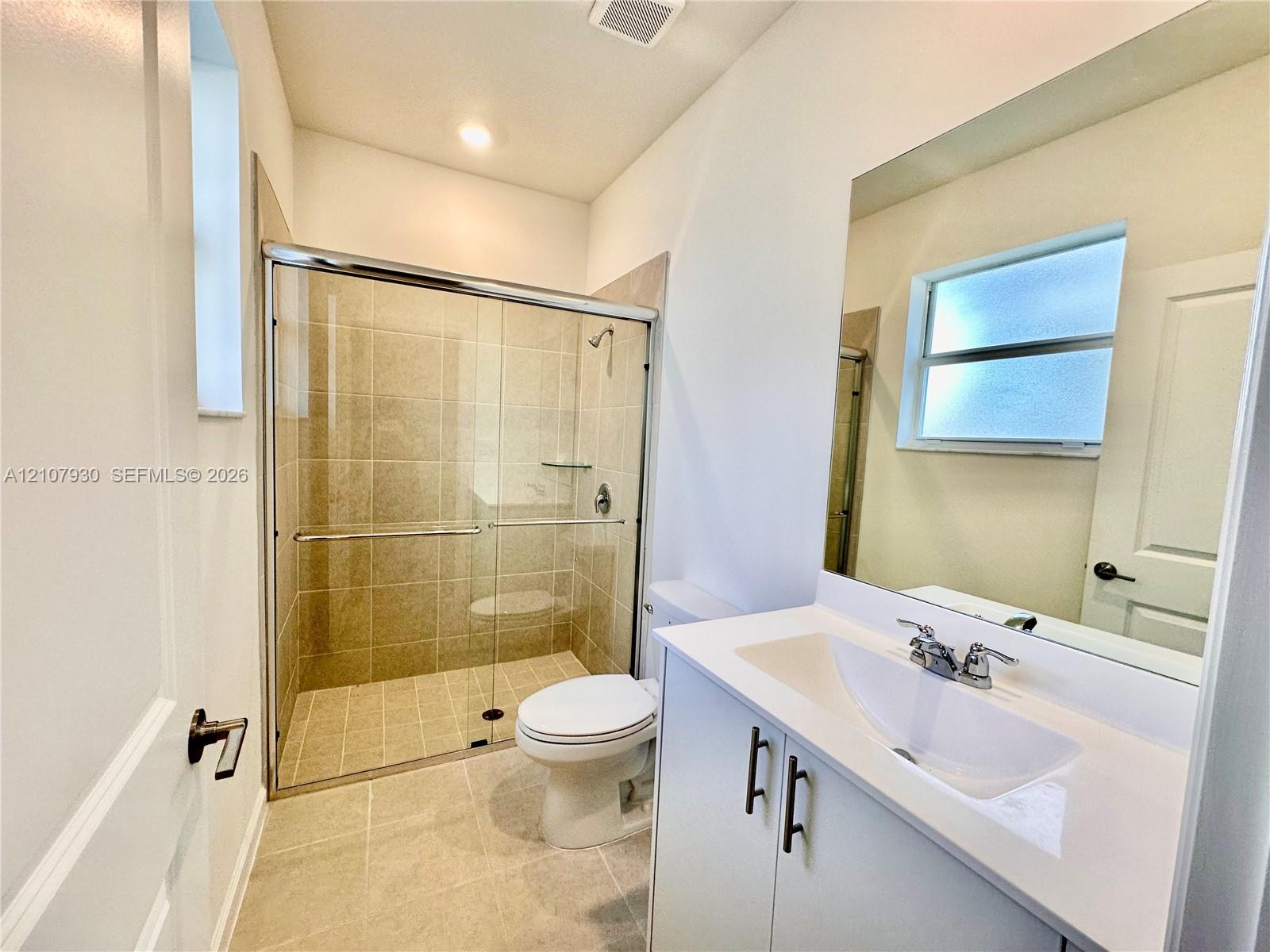 Bathroom featuring a glass-enclosed shower with tile surround, white vanity cabinet with a stone-composite countertop, undermount sink, and large wall-mounted mirror
