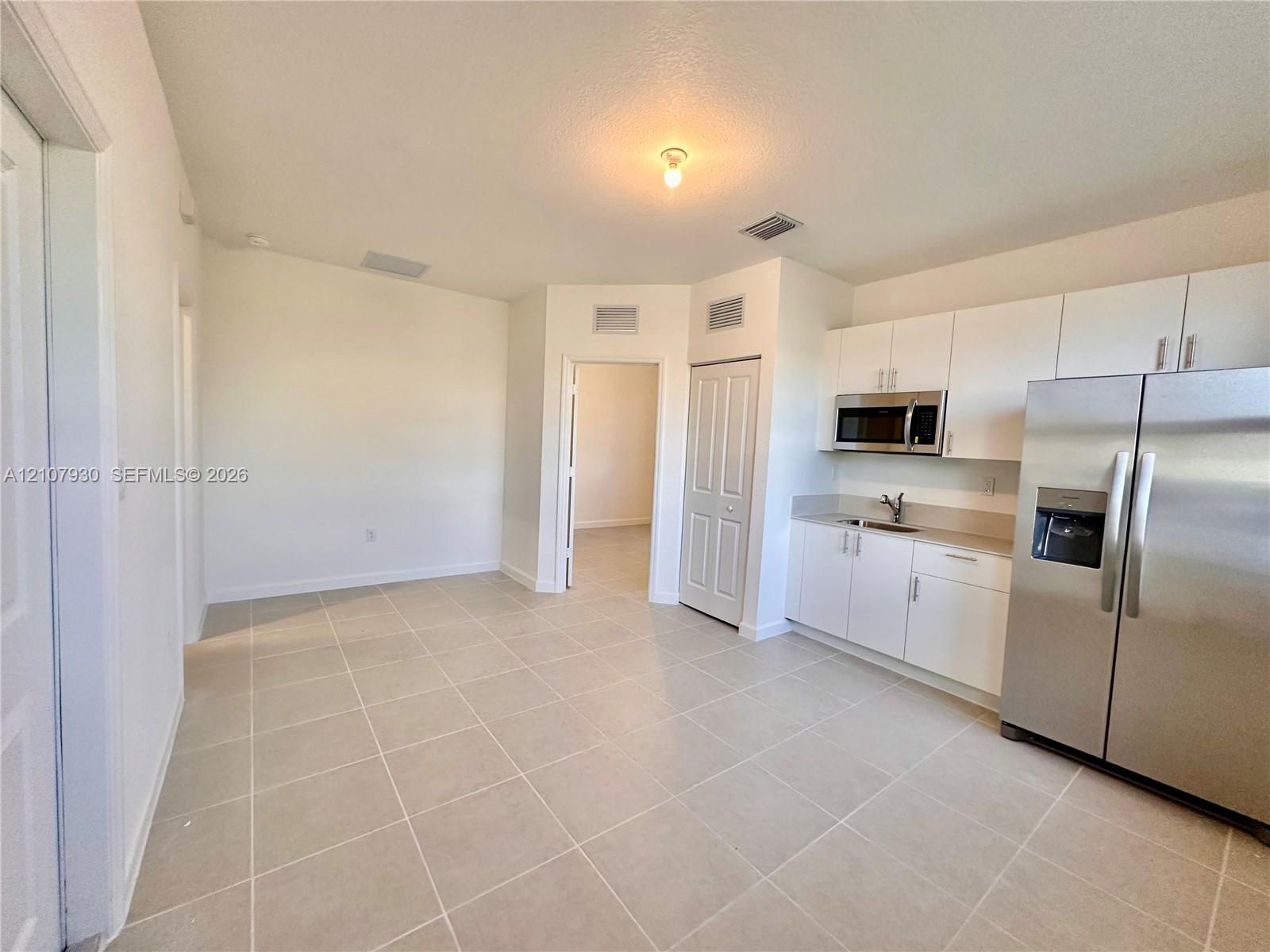 Kitchen area featuring white cabinetry, stainless steel refrigerator, built-in microwave, and tile flooring