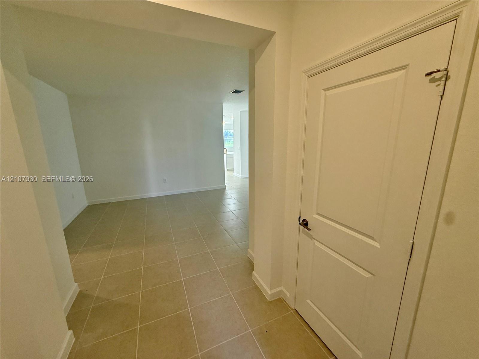 Interior entry featuring large-format ceramic tile flooring, neutral wall finishes, and a single-panel interior door with brushed metal hardware Interior entry featuring large-format ceramic tile flooring, neutral wall finishes, and a single-panel interior door with brushed metal hardware